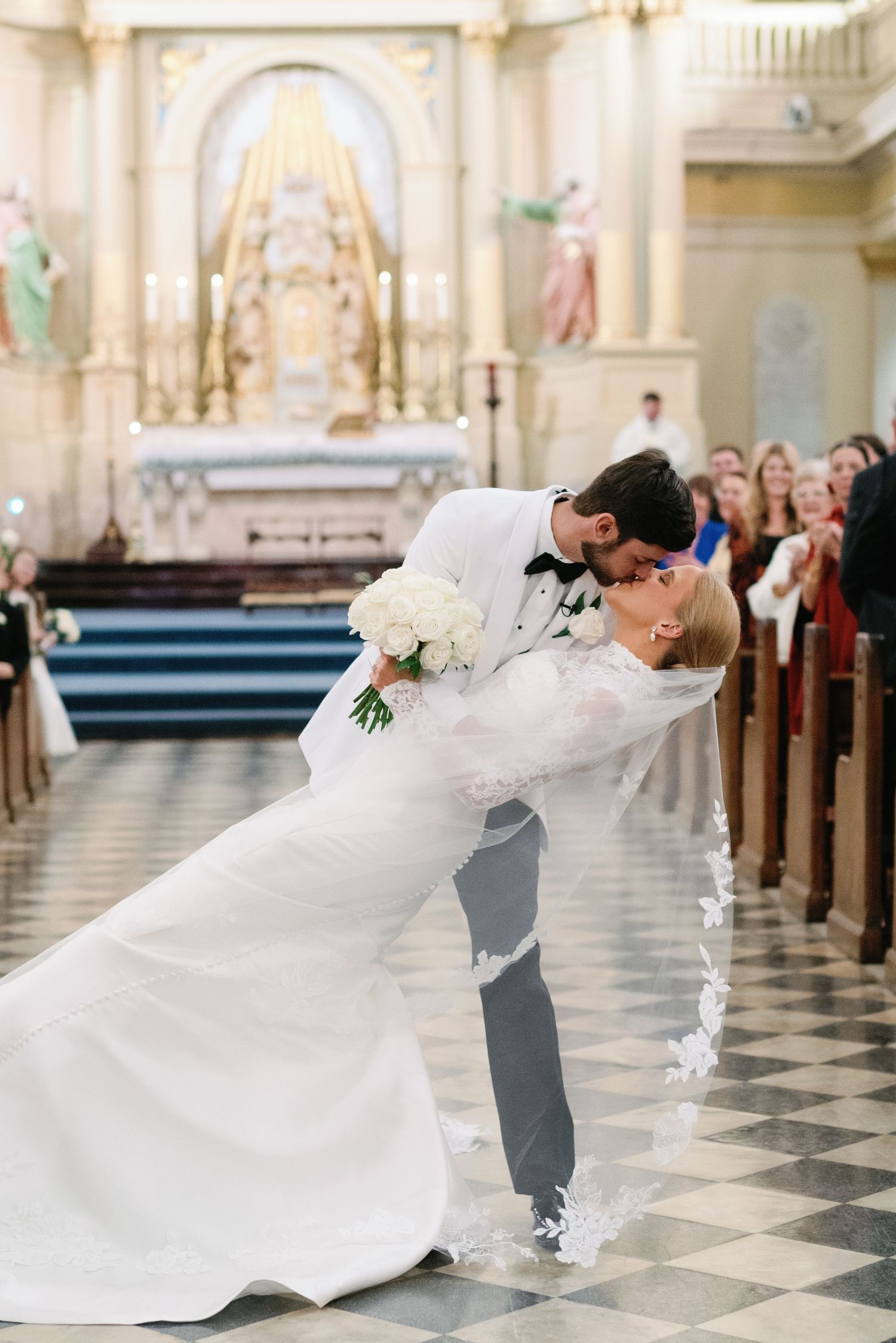 Couple performs dramatic dip pose on church's checkered floor during wedding photos.
