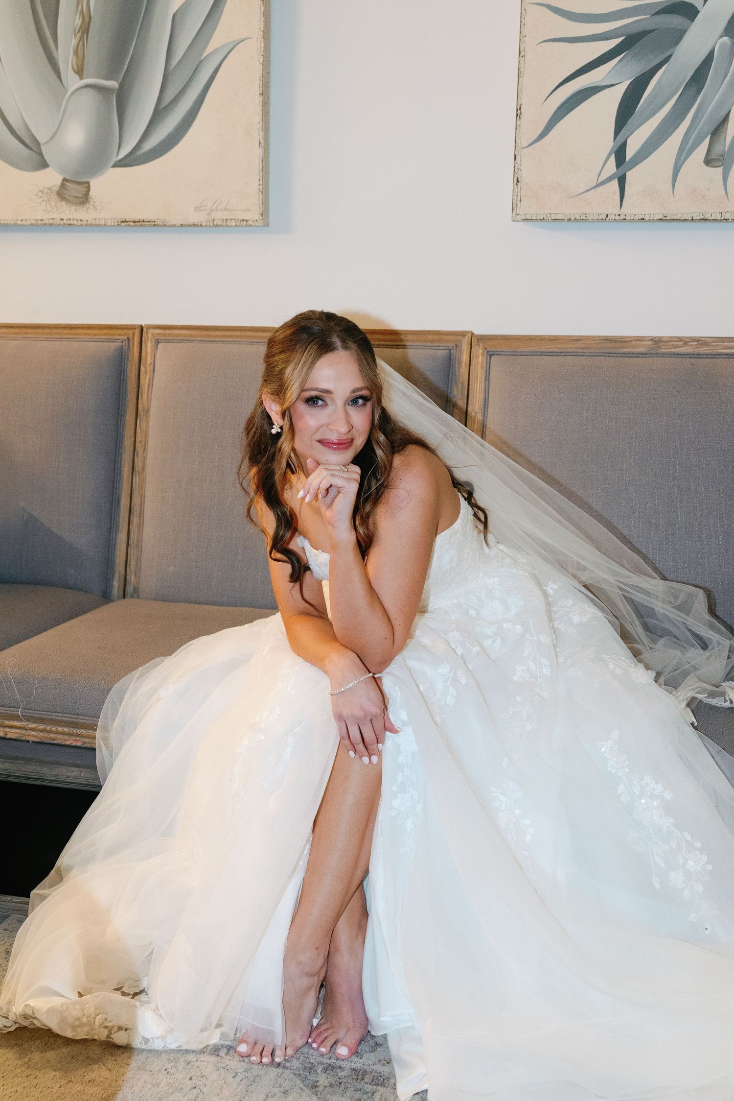 Bride in flowing white ballgown relaxes indoors against modern grey and white decor.
