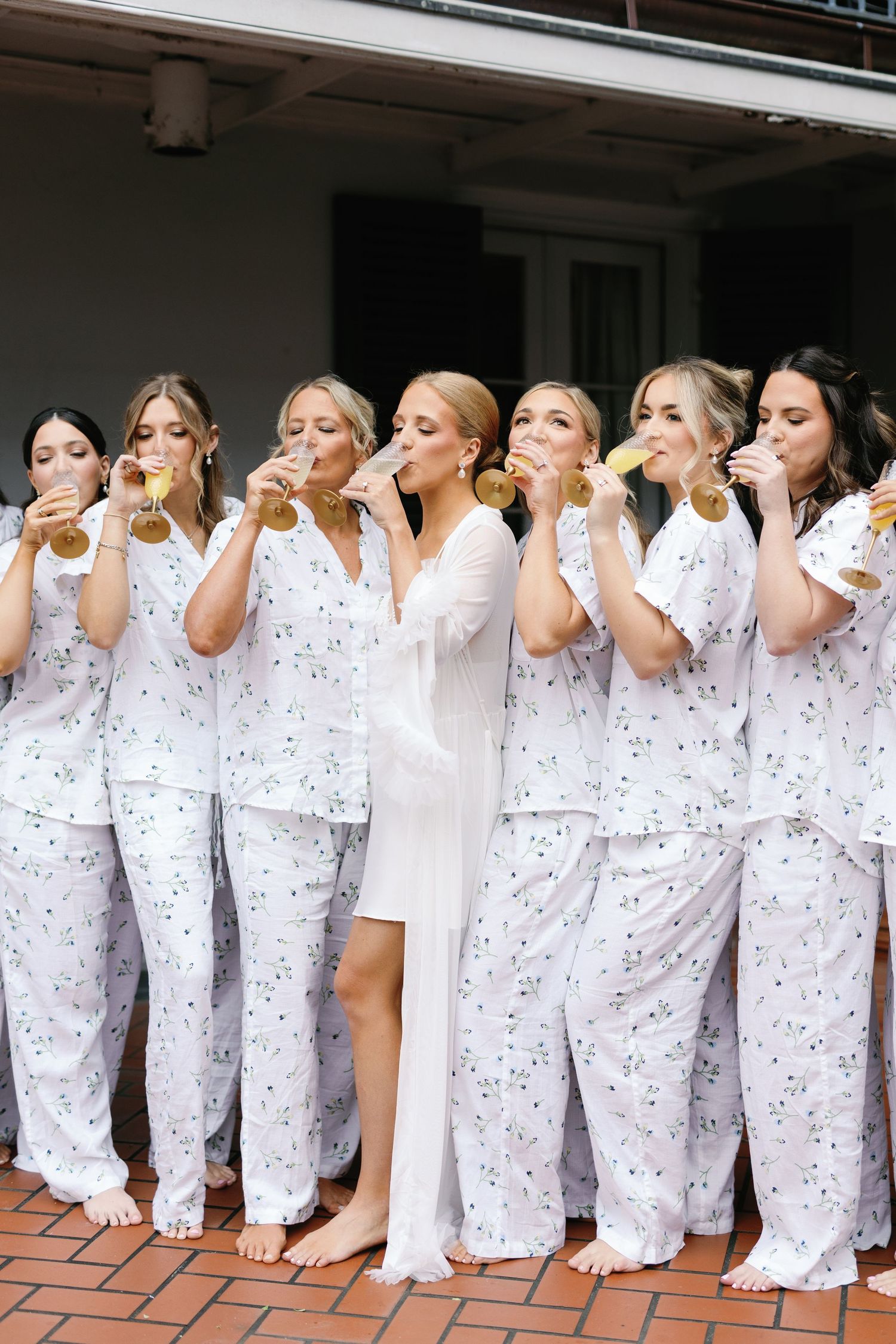 A group of people in matching white polka dot pajamas stand in a row taking a synchronized drinking photo.