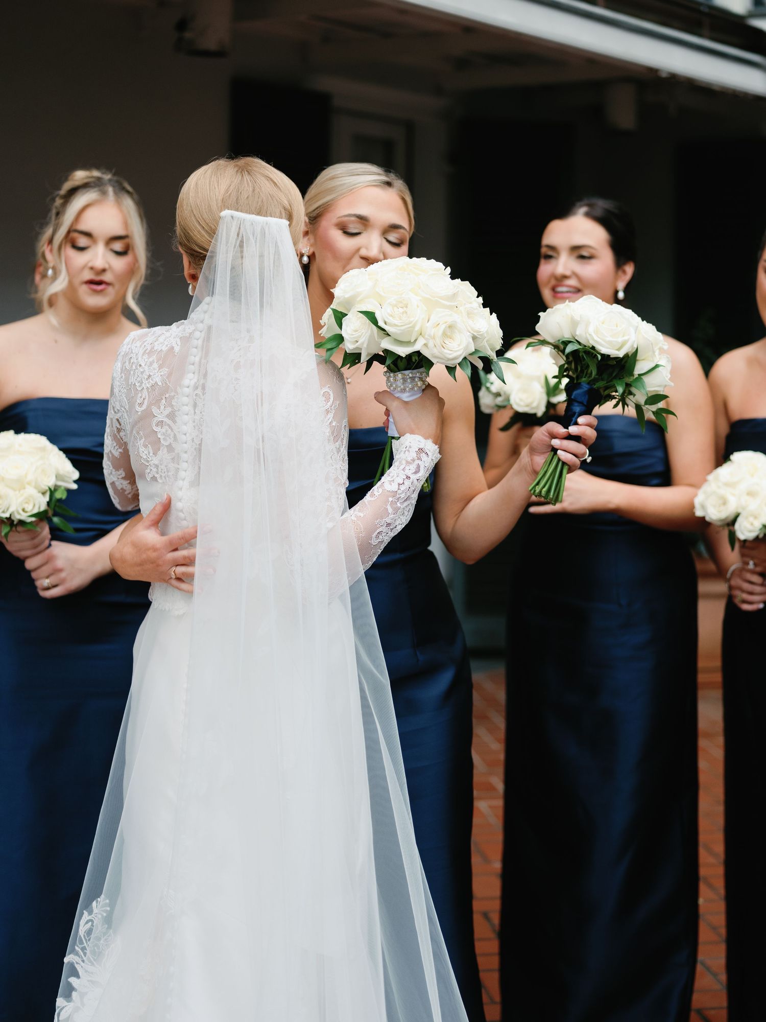 Bridesmaids in navy blue dresses hold white bouquets while posing for wedding photos.