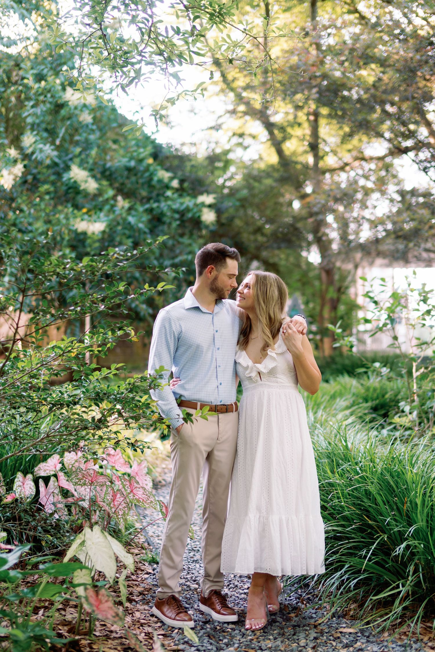 A romantic couple shares tender moments in a lush garden setting with blooming flowers and greenery.