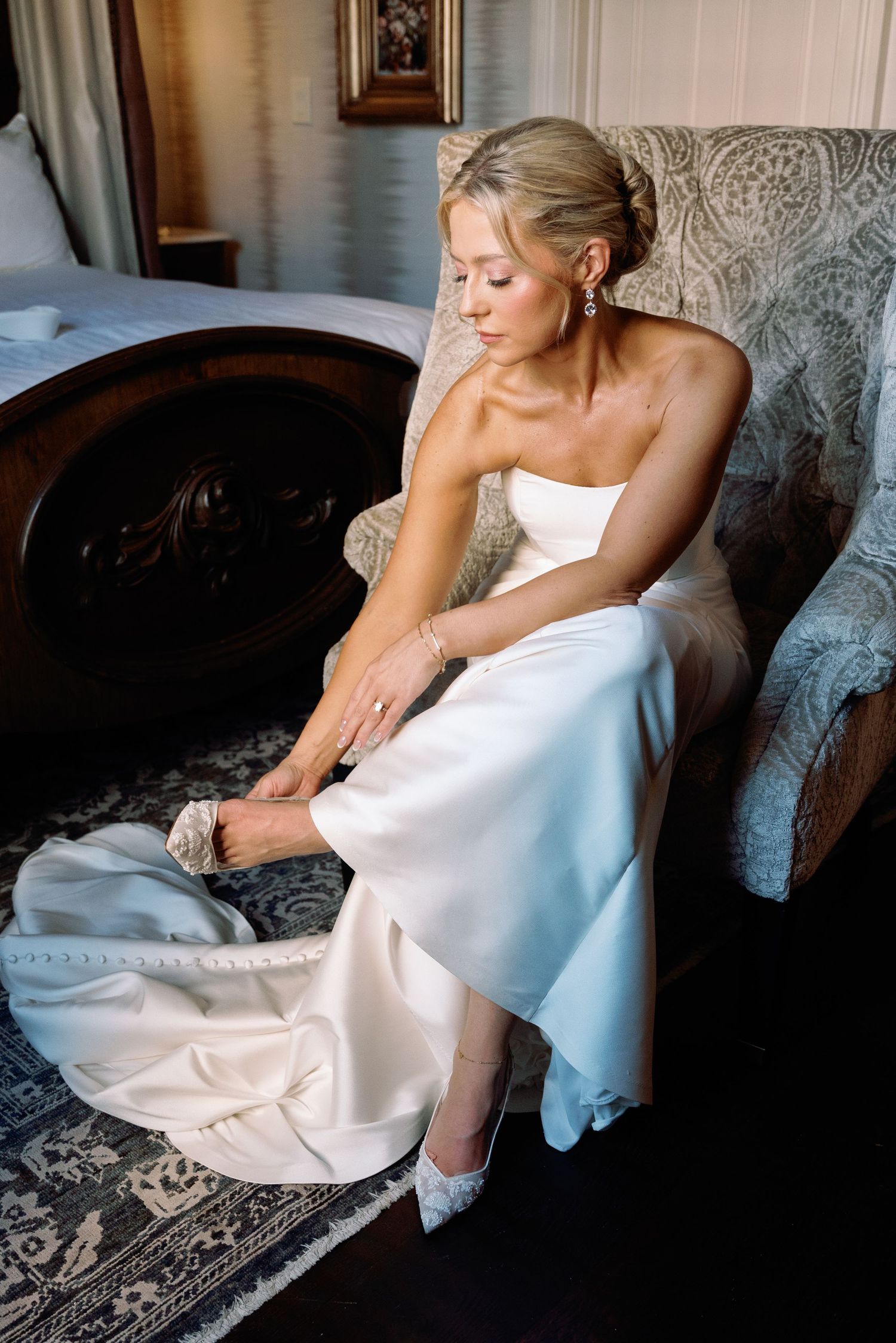 Bride in white wedding gown reclining on vintage upholstered chair.