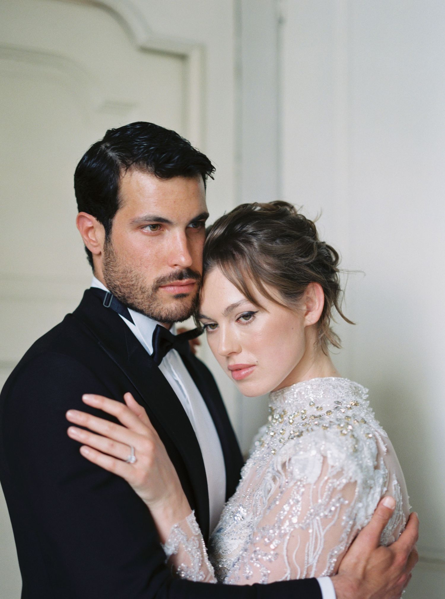 Elegant wedding couple embracing in a light-filled room with ornate white walls.