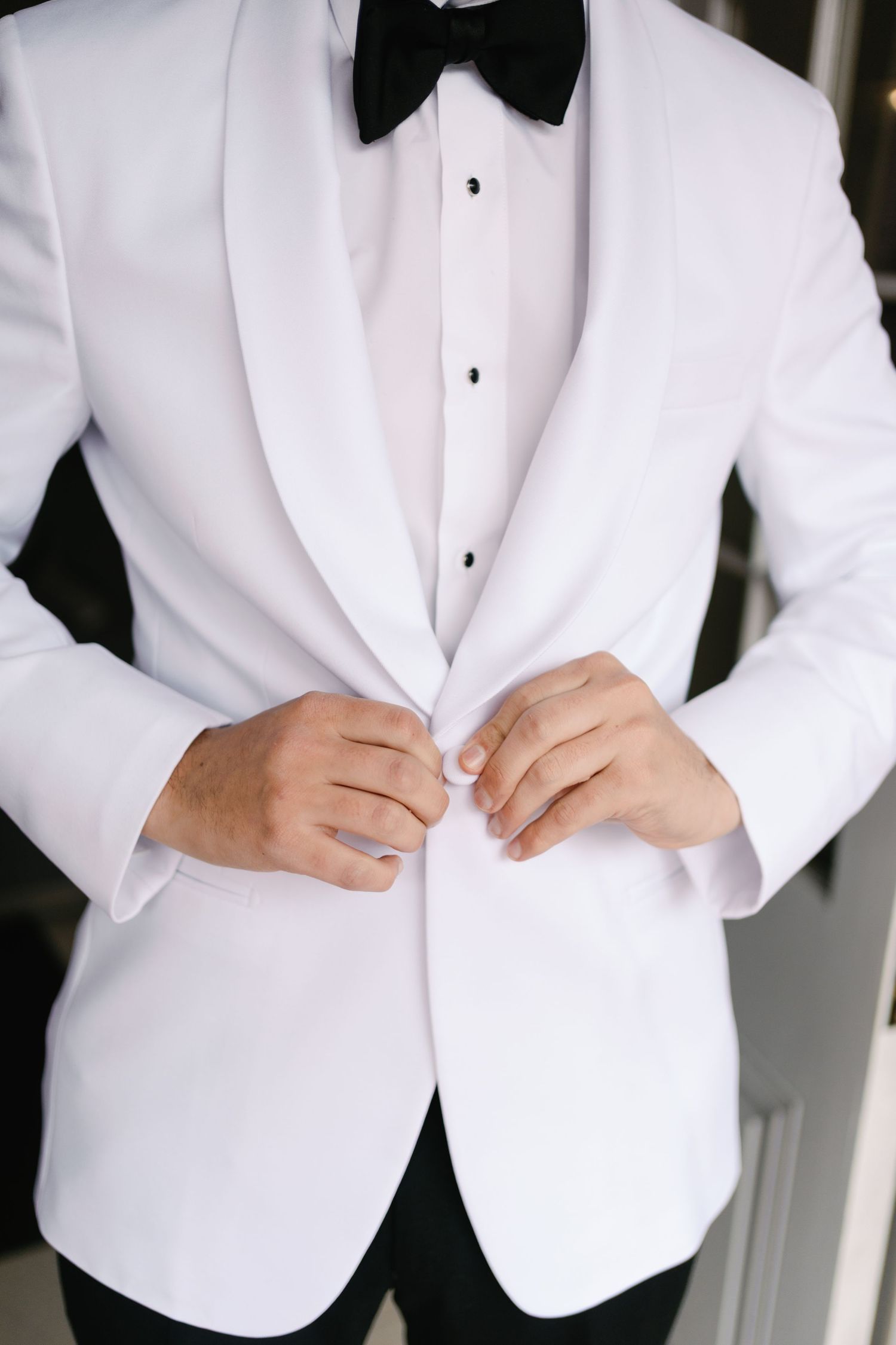 Close-up shots of groom adjusting white tuxedo jacket and bow tie.