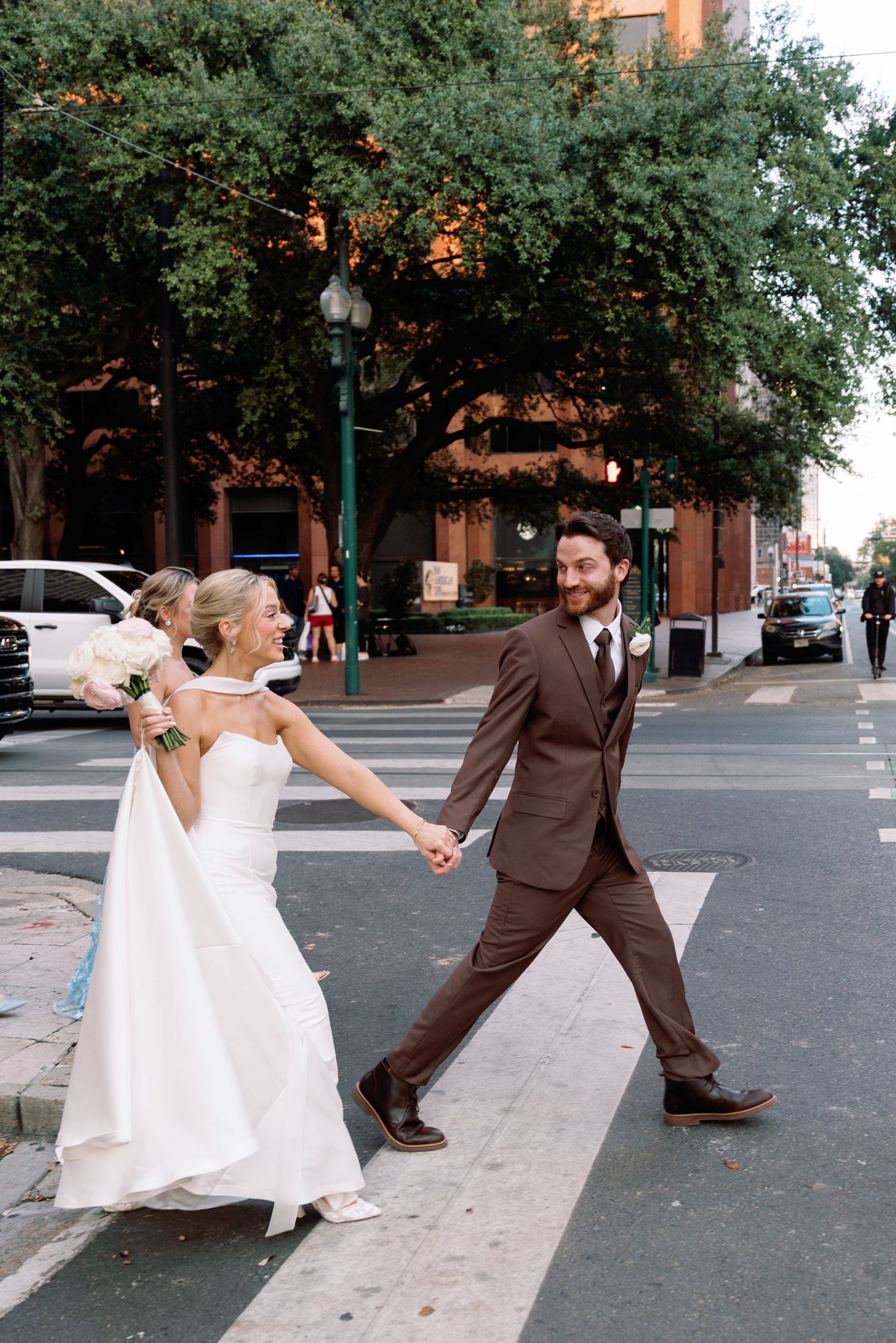Playful wedding couple performs dance moves on city street.