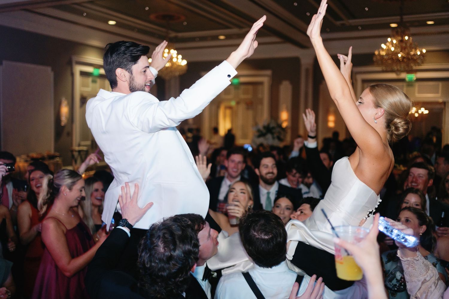 People dancing and celebrating at a wedding reception with their hands raised in a joyful atmosphere.
