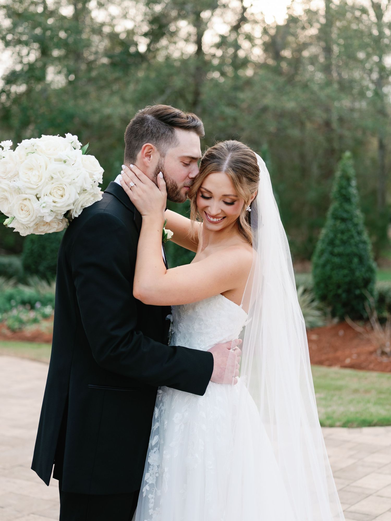 Newlyweds share intimate embrace during outdoor wedding photoshoot on stone pathway.