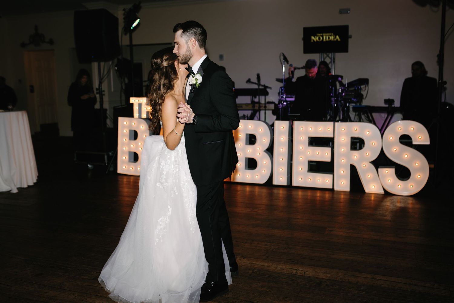 A couple shares their first dance at a wedding reception with illuminated letter decor.