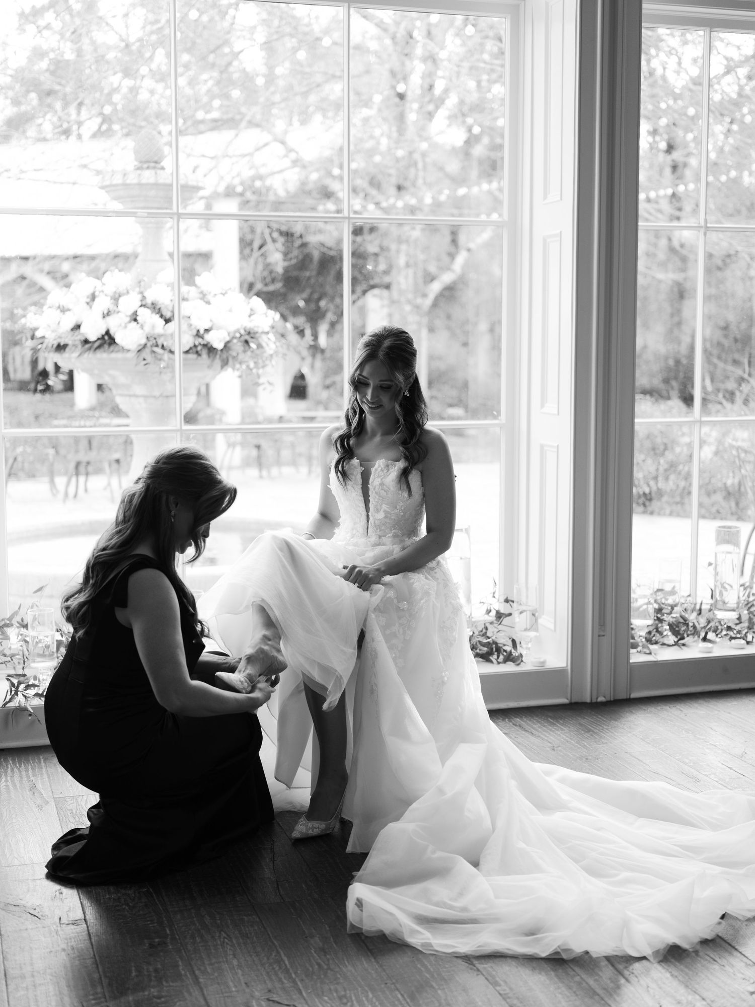 Black and white photo series showing bride in flowing white gown getting ready in sunlit room with bridesmaids.