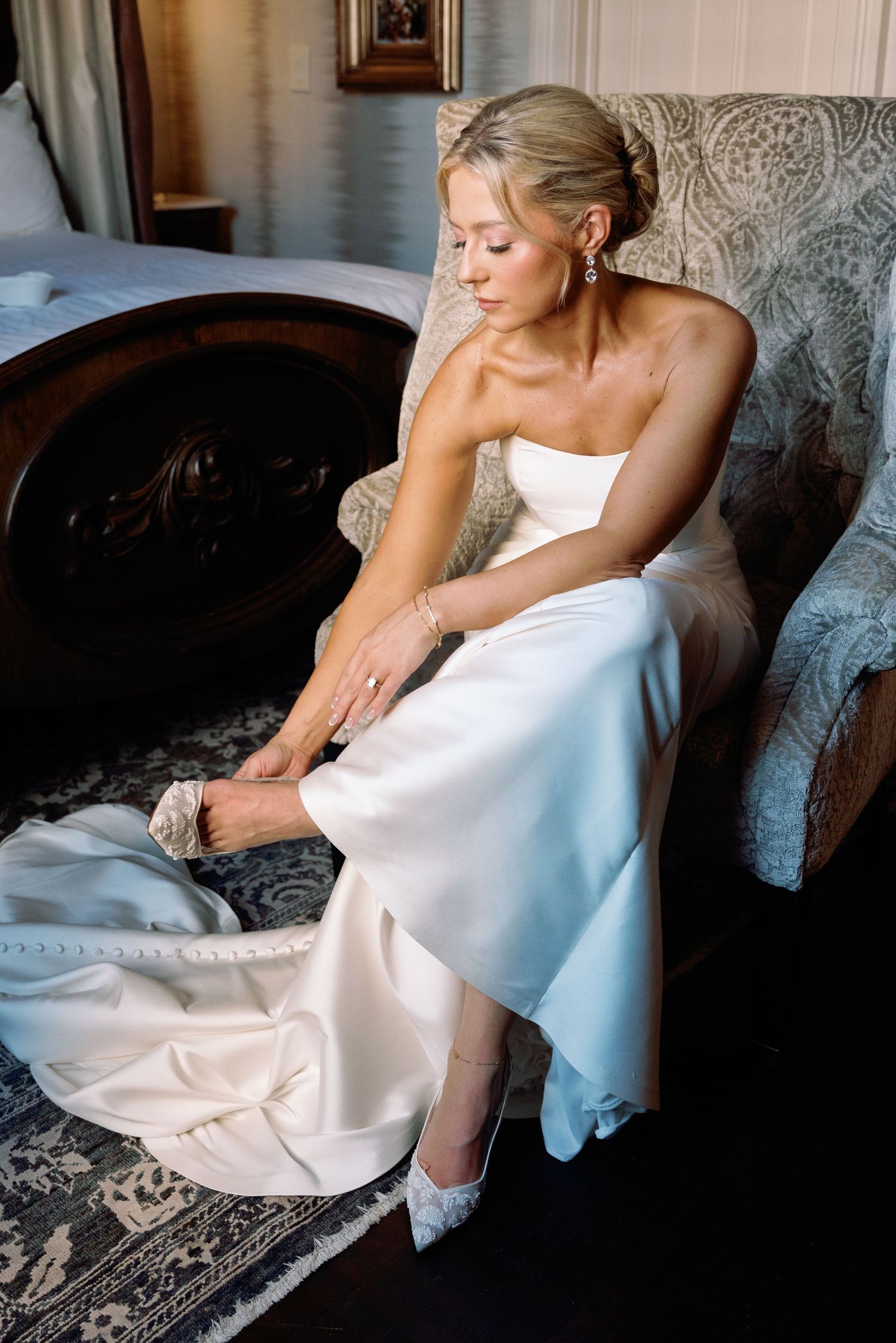 Elegant bride in white dress reclines on vintage chaise lounge during wedding day photoshoot.