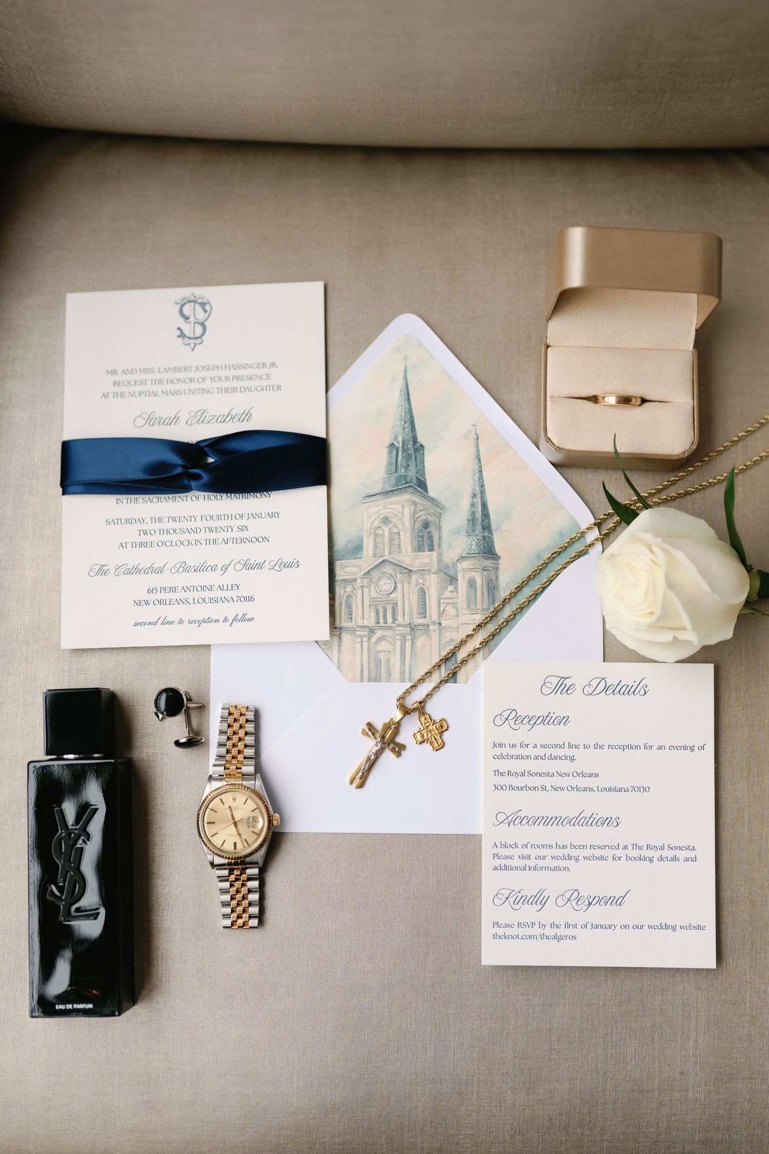 Elegant wedding details including invitations, rings, watch, and other accessories arranged on a neutral background.