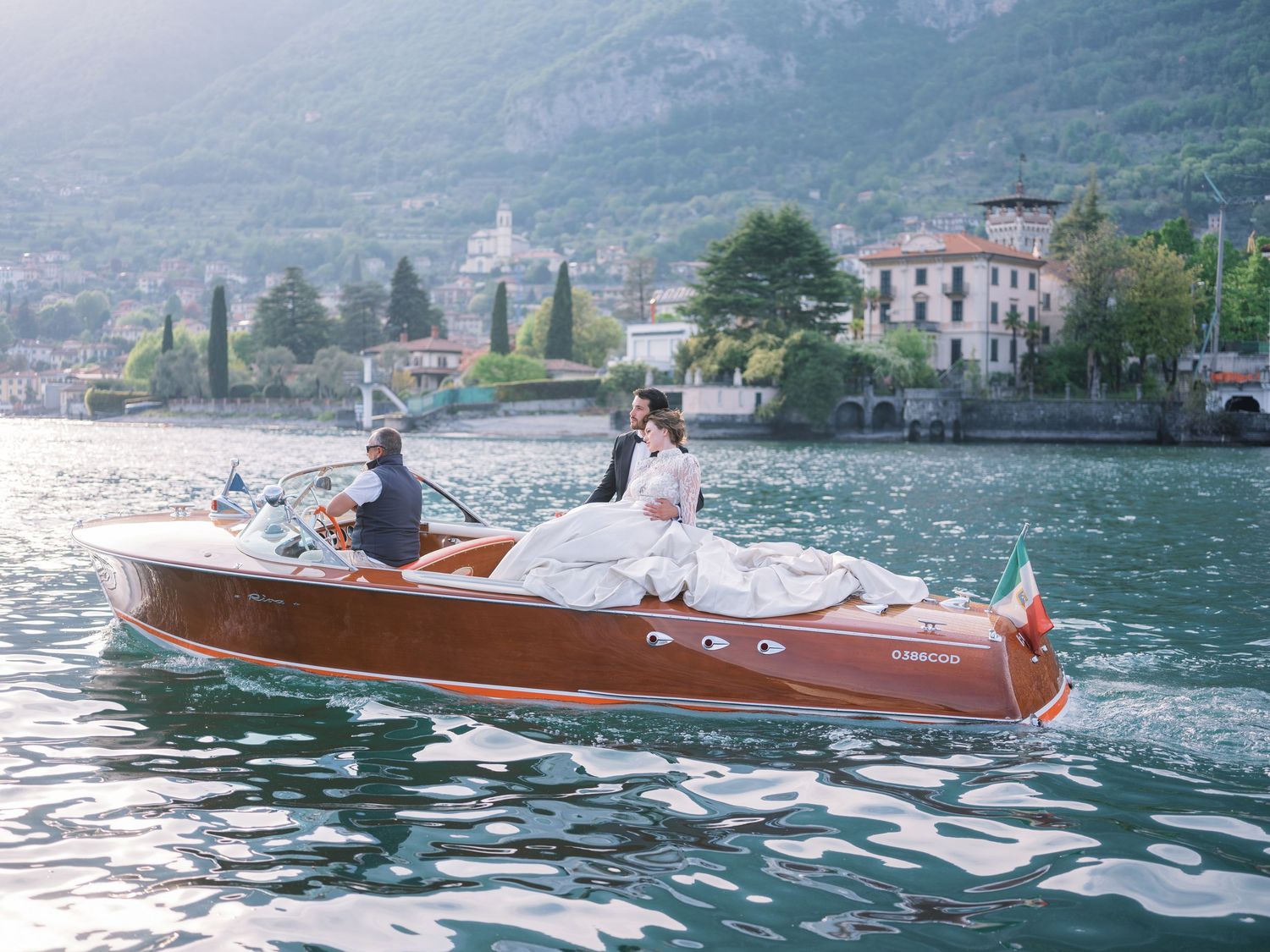 Classic wooden speedboat cruising on Lake Como with mountains in background.