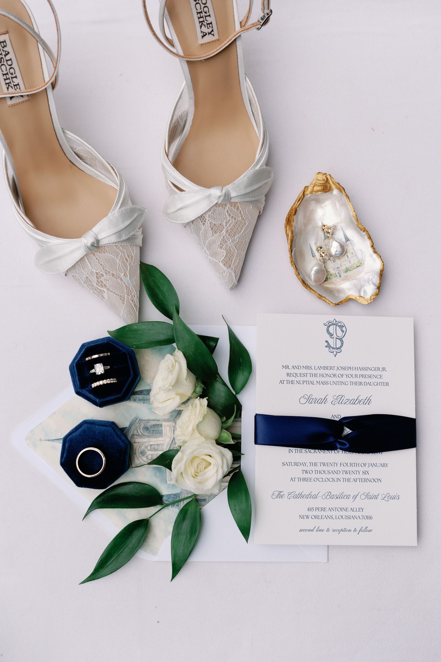 Elegant white lace wedding shoes with wedding invitation and white roses on light background.