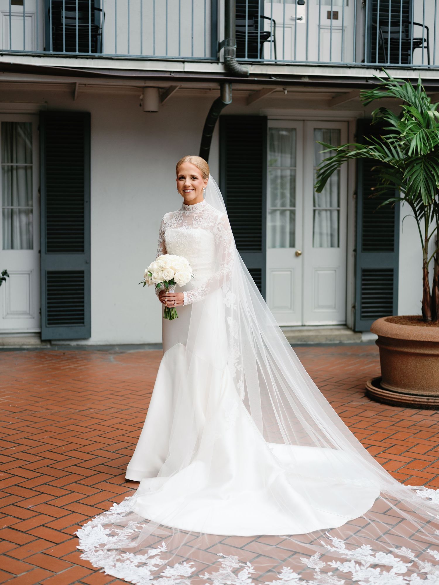 A flowing white wedding dress with long train displayed on terracotta tiles in a courtyard setting.