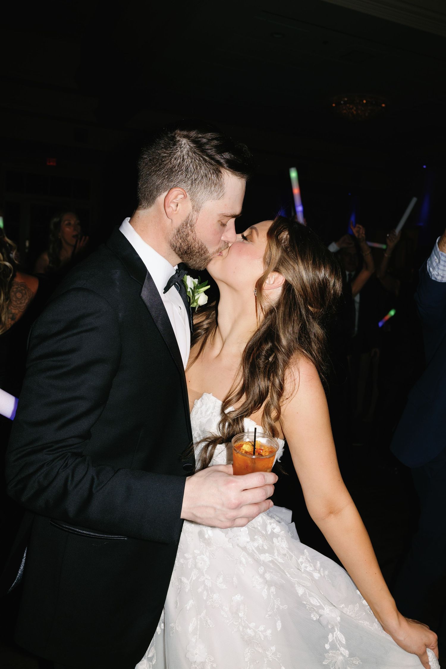 Couple shares romantic dance moment at dimly lit wedding reception with colorful lights.