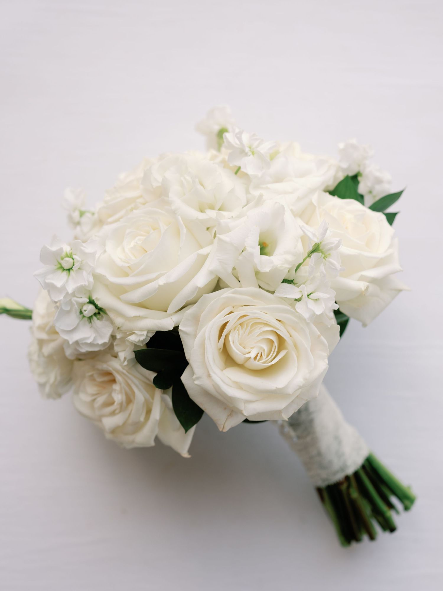 Elegant white rose bridal bouquet wrapped in ribbon against light background.