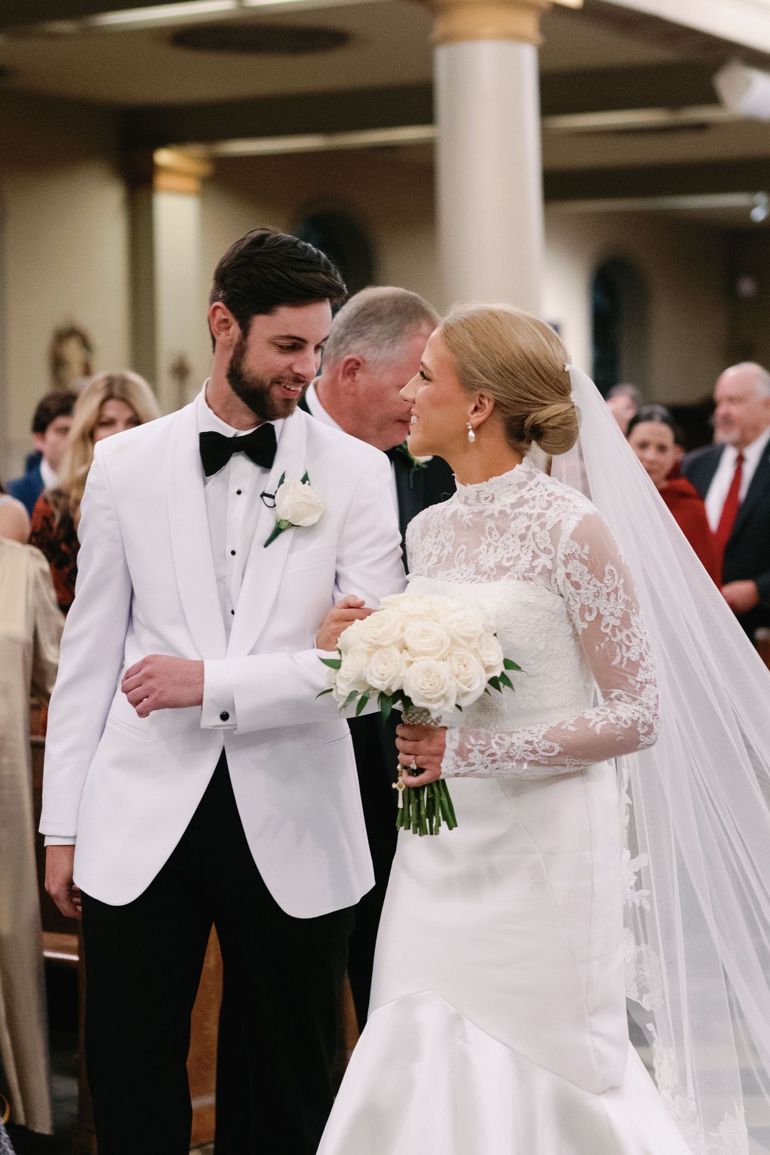 Wedding ceremony in a church with white floral arrangements and formal attire.