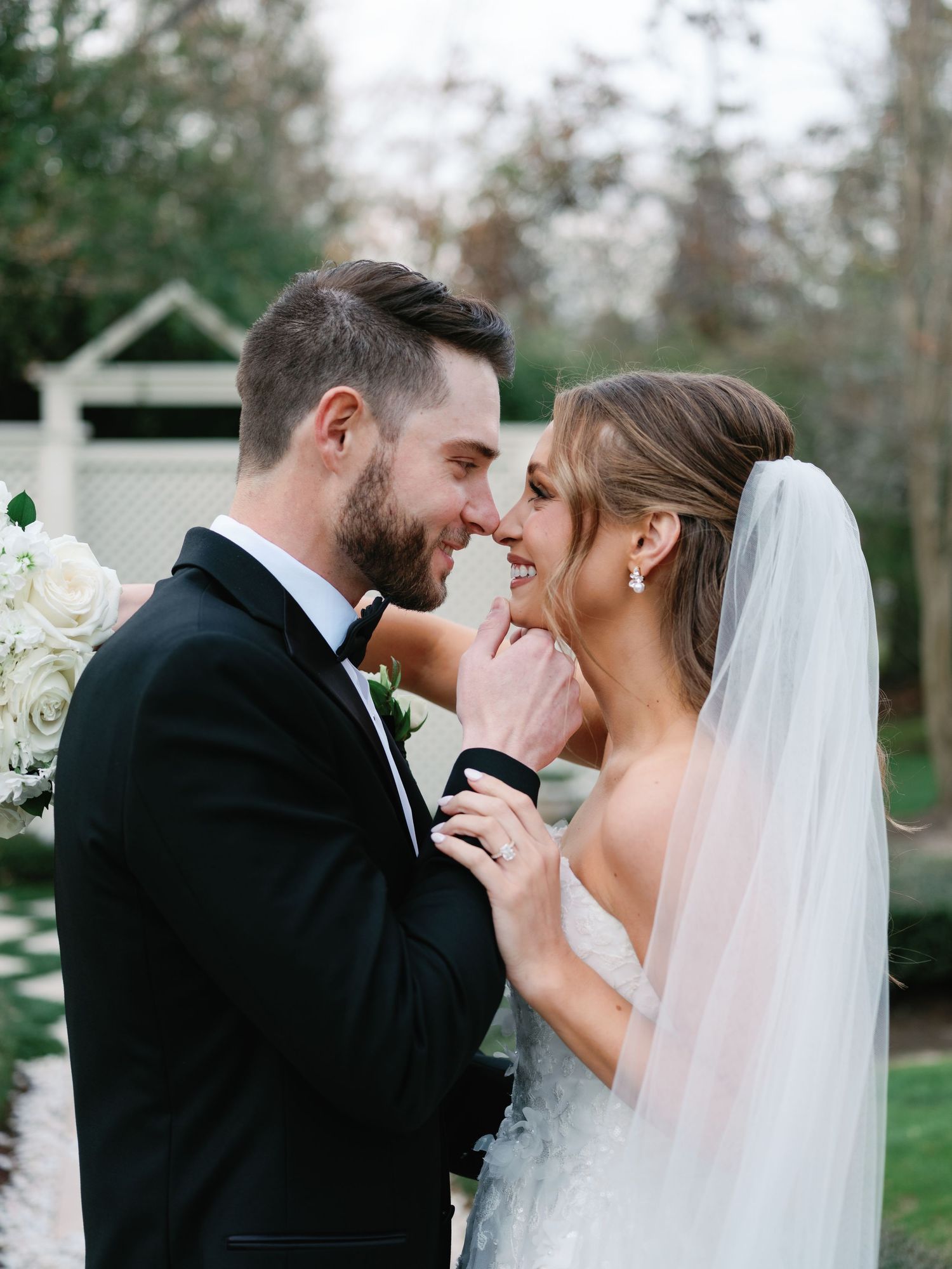 A tender moment between newlyweds outdoors with white floral arrangements.