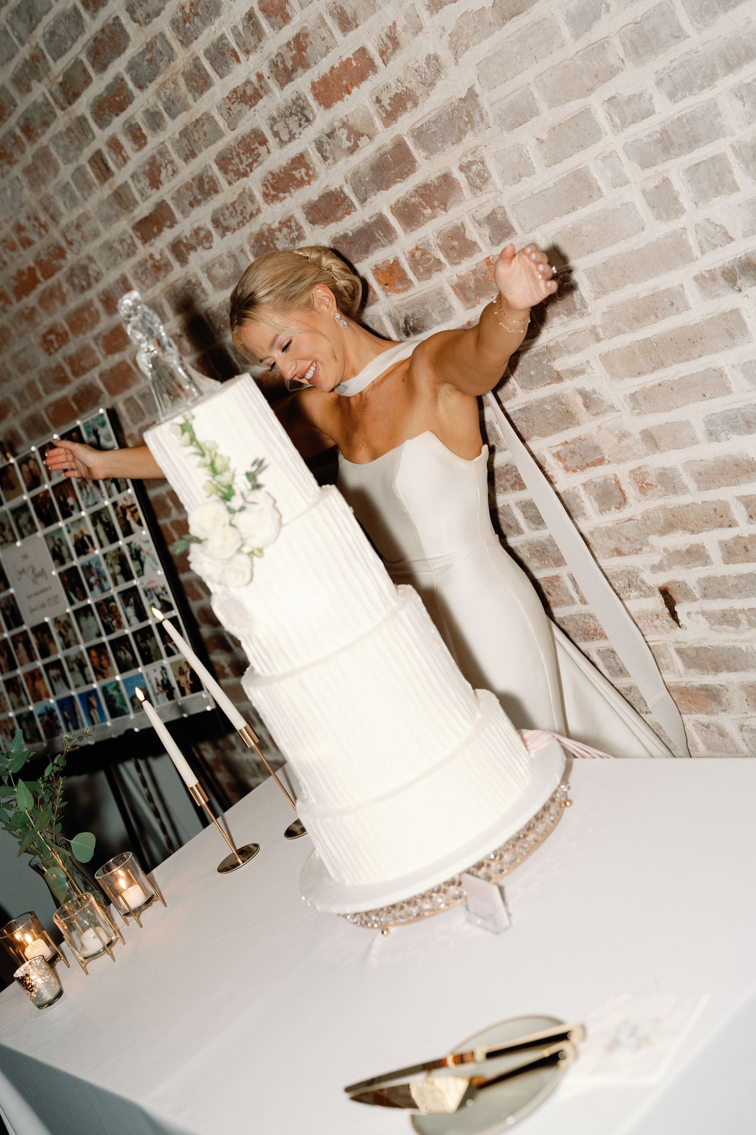 A classic white tiered wedding cake displayed against a brick wall backdrop.