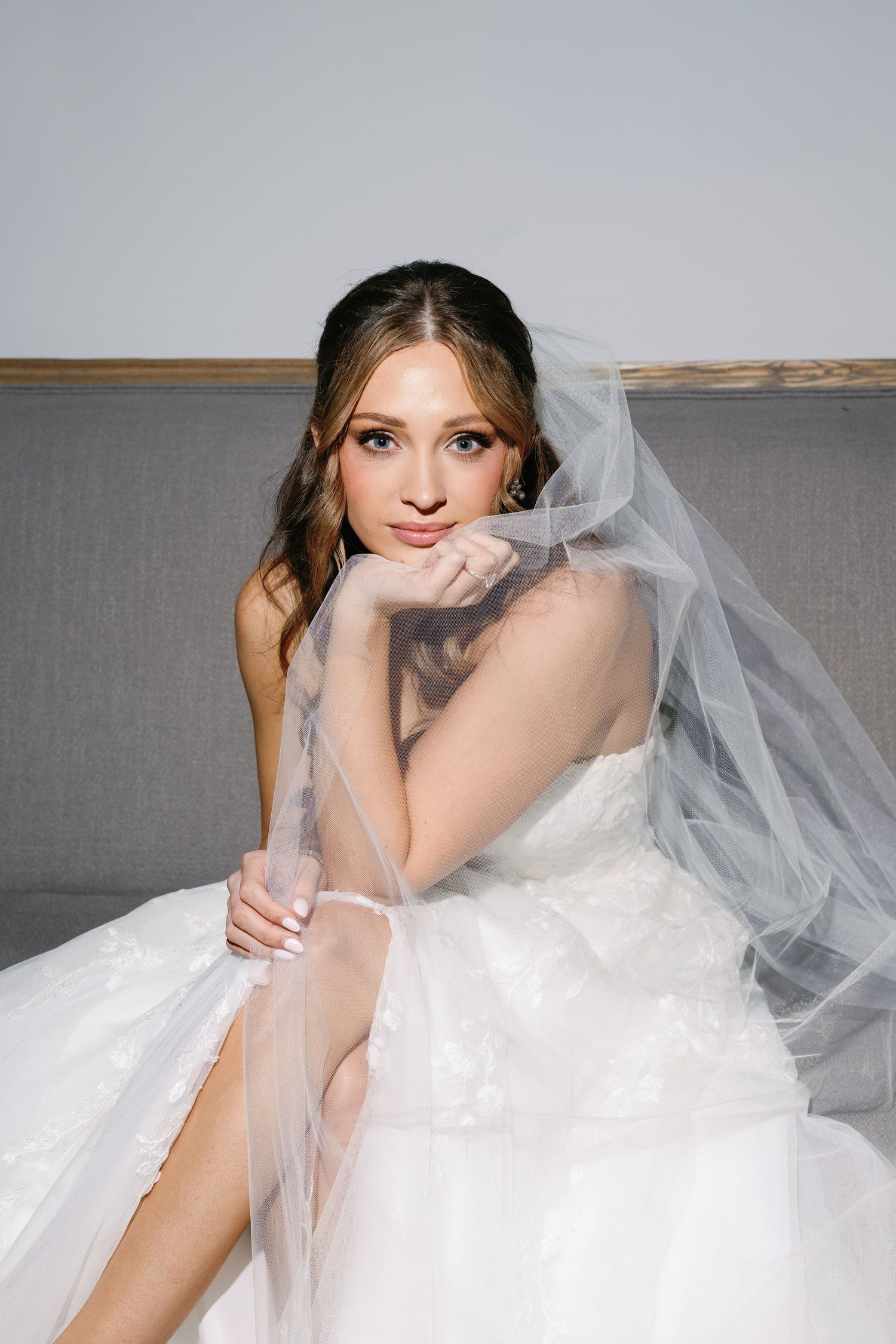 Bride in white wedding dress and veil poses elegantly against a grey backdrop.