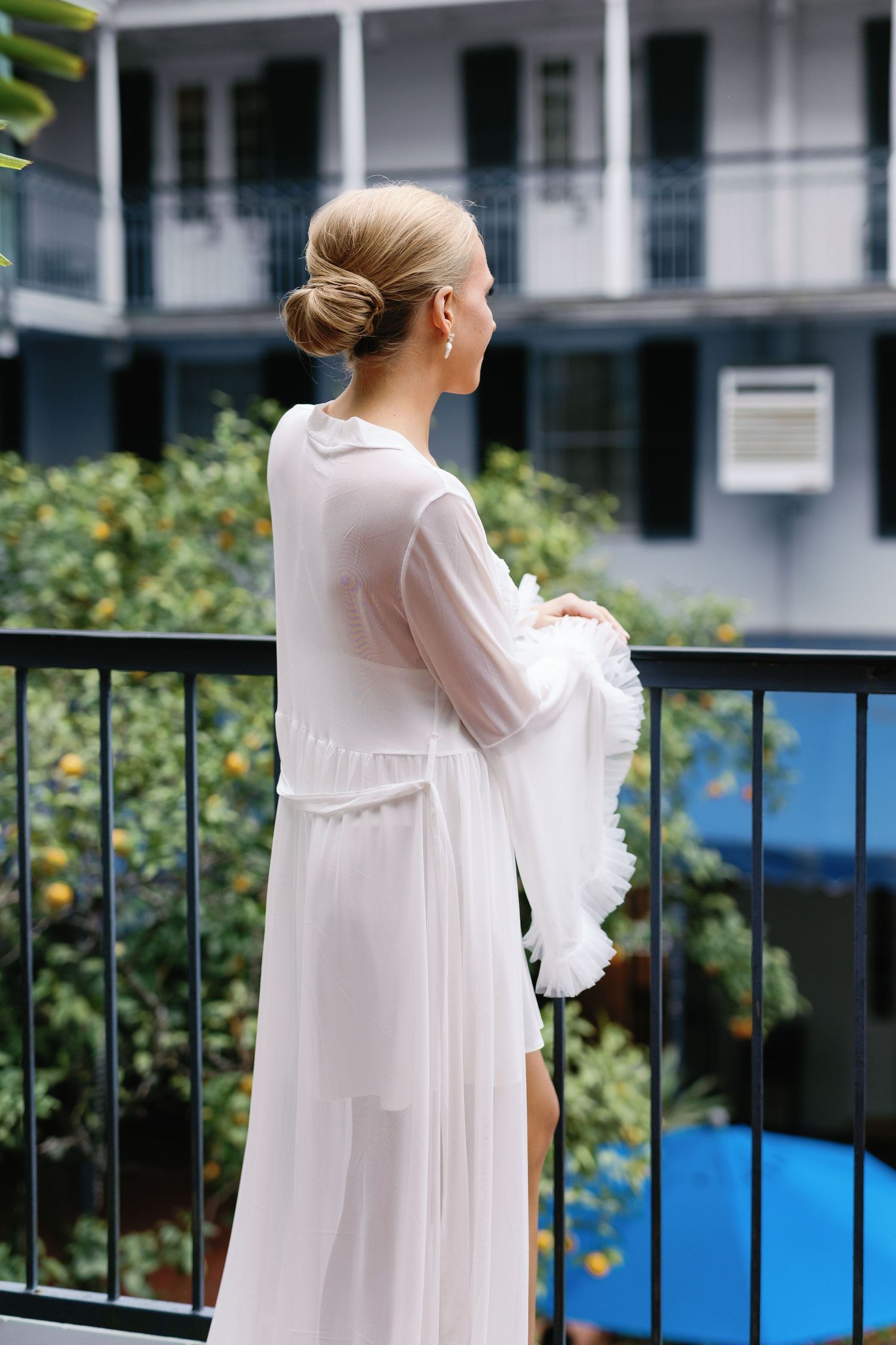 A flowing white bridal robe is showcased against an outdoor balcony setting.
