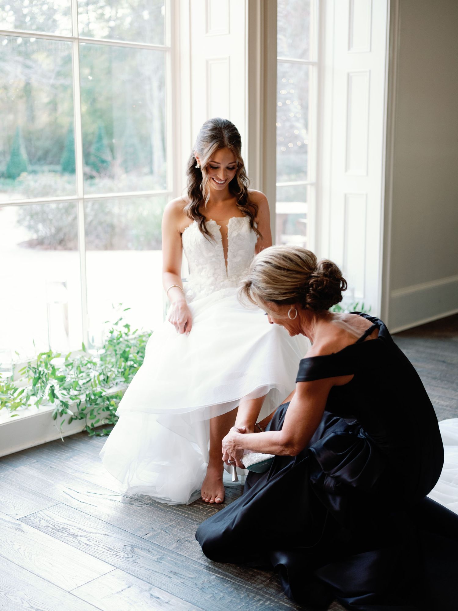 Wedding preparation scene with flowing white dress against bright windows.