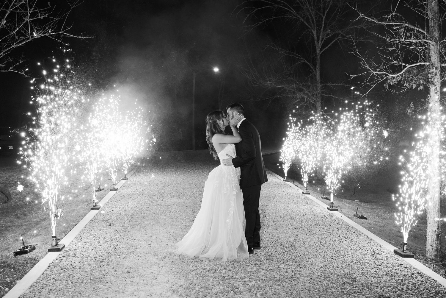 Sparklers illuminate a nighttime wedding celebration with glowing light trails against a dark background.