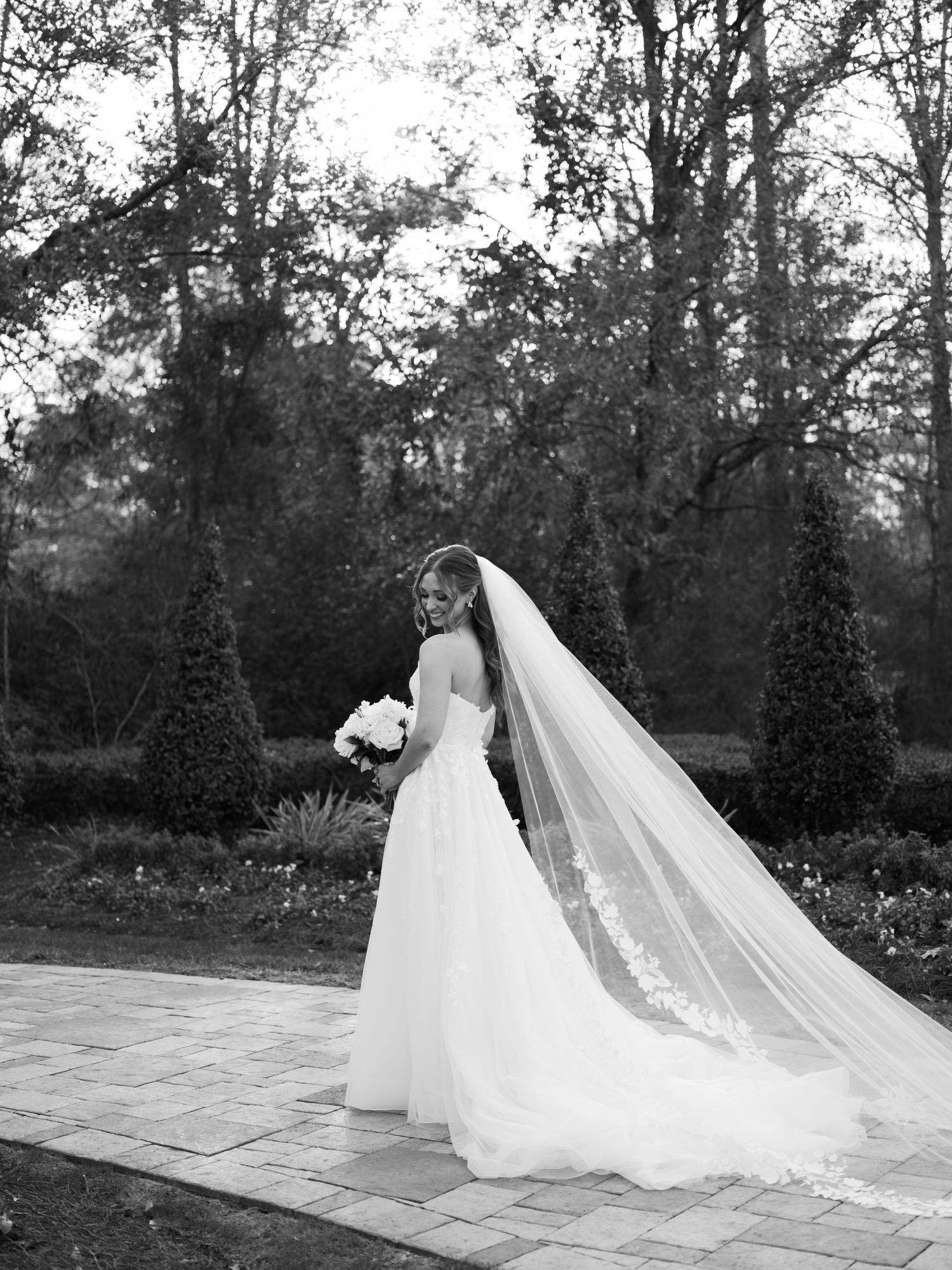 Dramatic black and white wedding portraits with flowing veil in an outdoor garden setting.