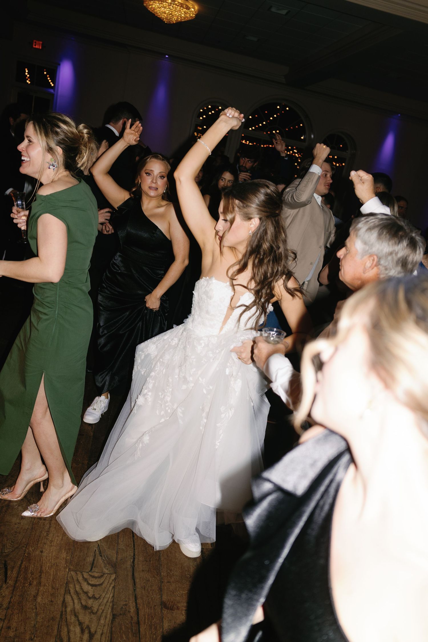Wedding reception dance floor filled with guests celebrating under dim lighting.