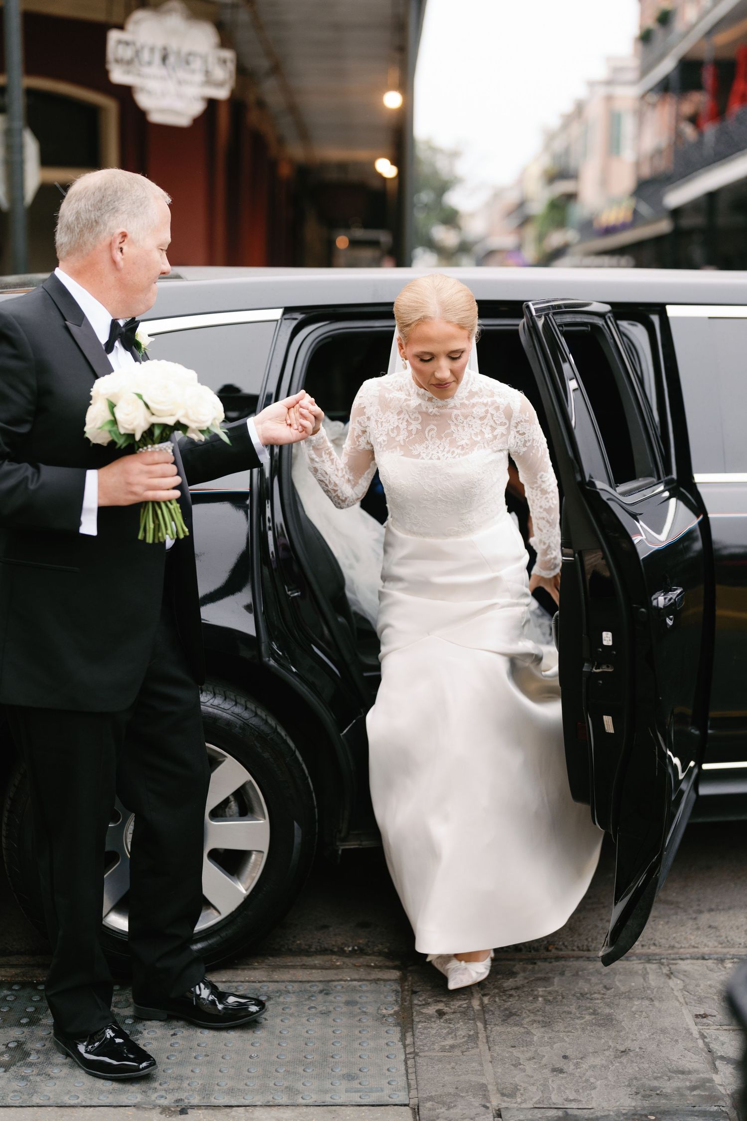 A sequence showing someone in a white dress being helped into a black car on a city street.