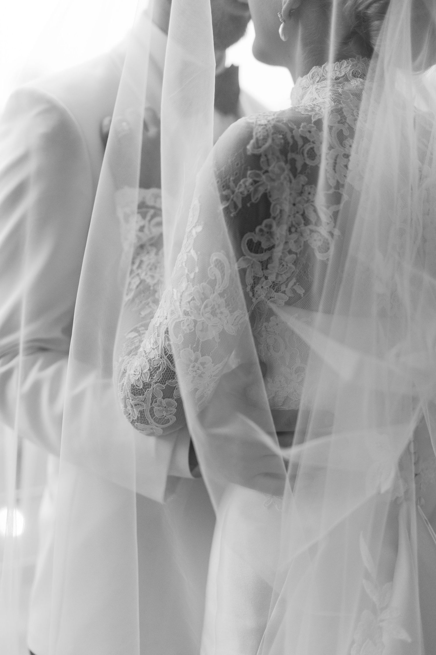 Close-up details of white lace wedding dress and veil in soft, ethereal lighting.