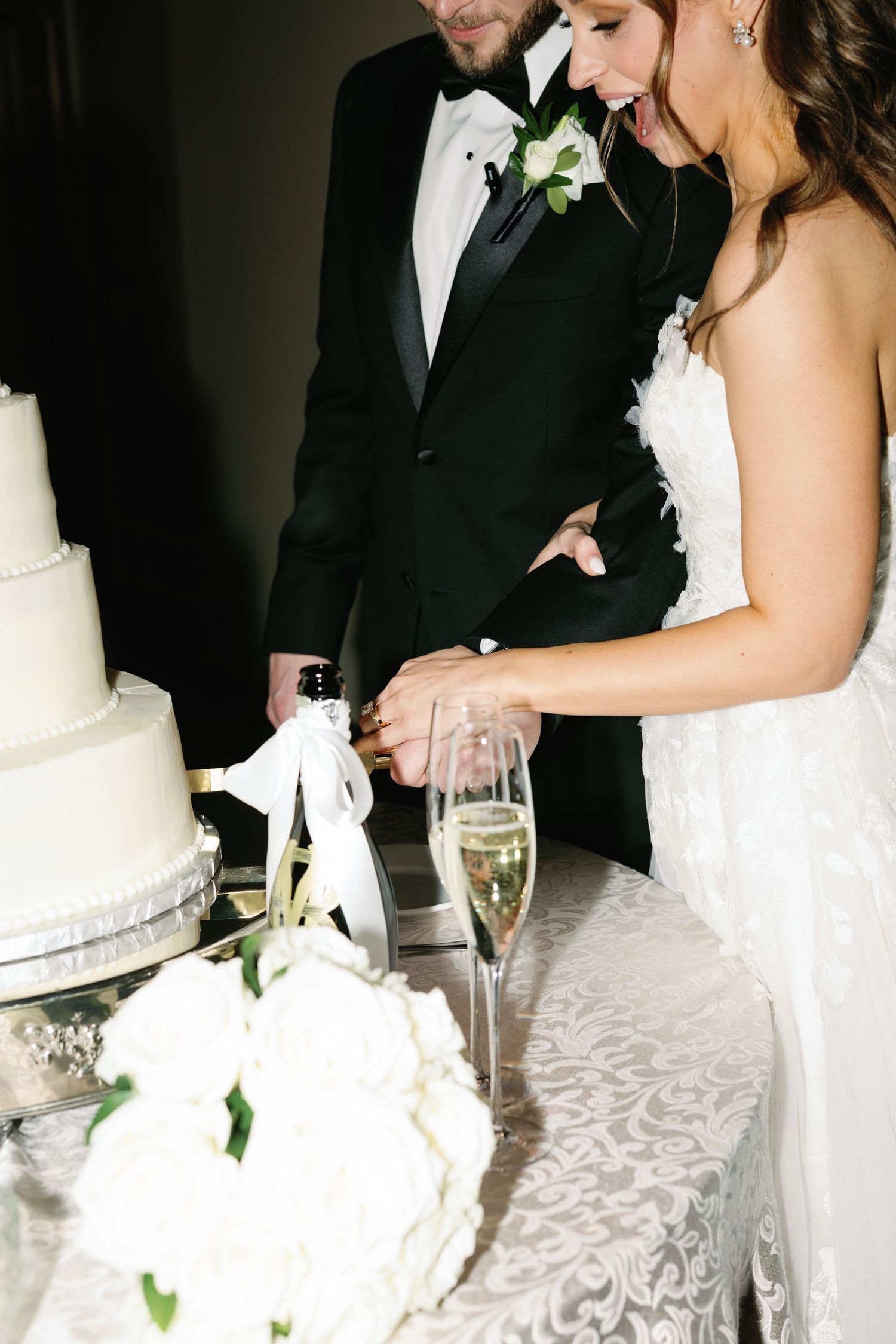 Couple cutting elegant white wedding cake with champagne flutes.