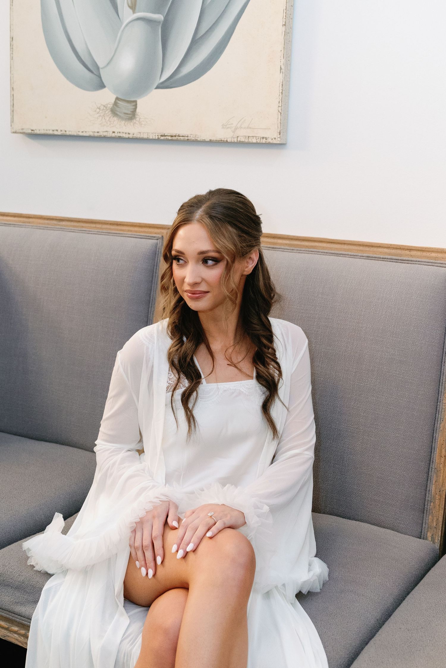 Wedding morning preparations on grey couch with white dress and decorative wall art.