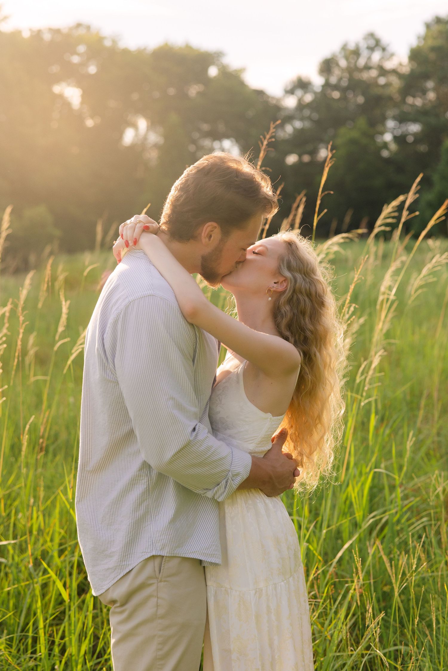 Emily and Harrison share a kiss in front of tall grass during golden hour at Hollow Creek Tree Farm in Gilbert, SC.