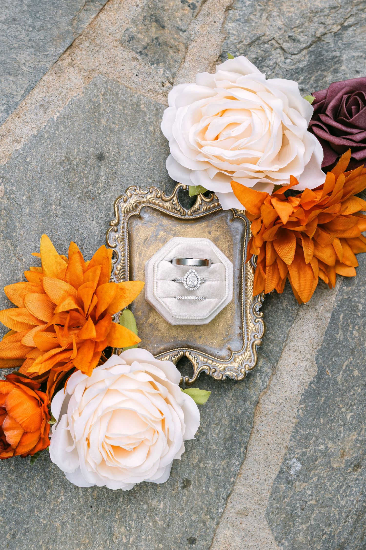 Wedding detail flat lay with white roses and orange florals styled on textured stone surface