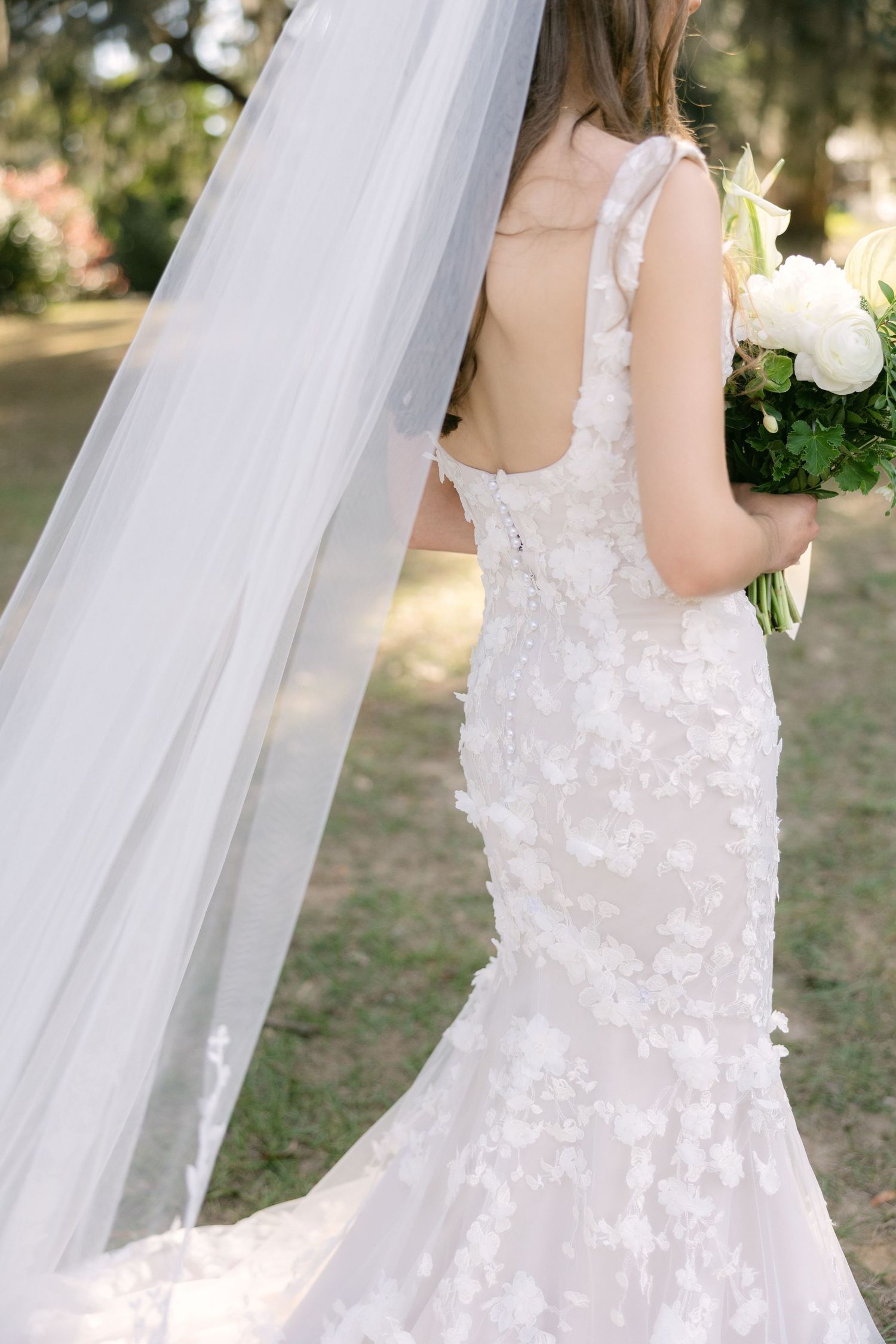 Bride walking outdoors with long veil flowing behind her during light and airy South Carolina wedding