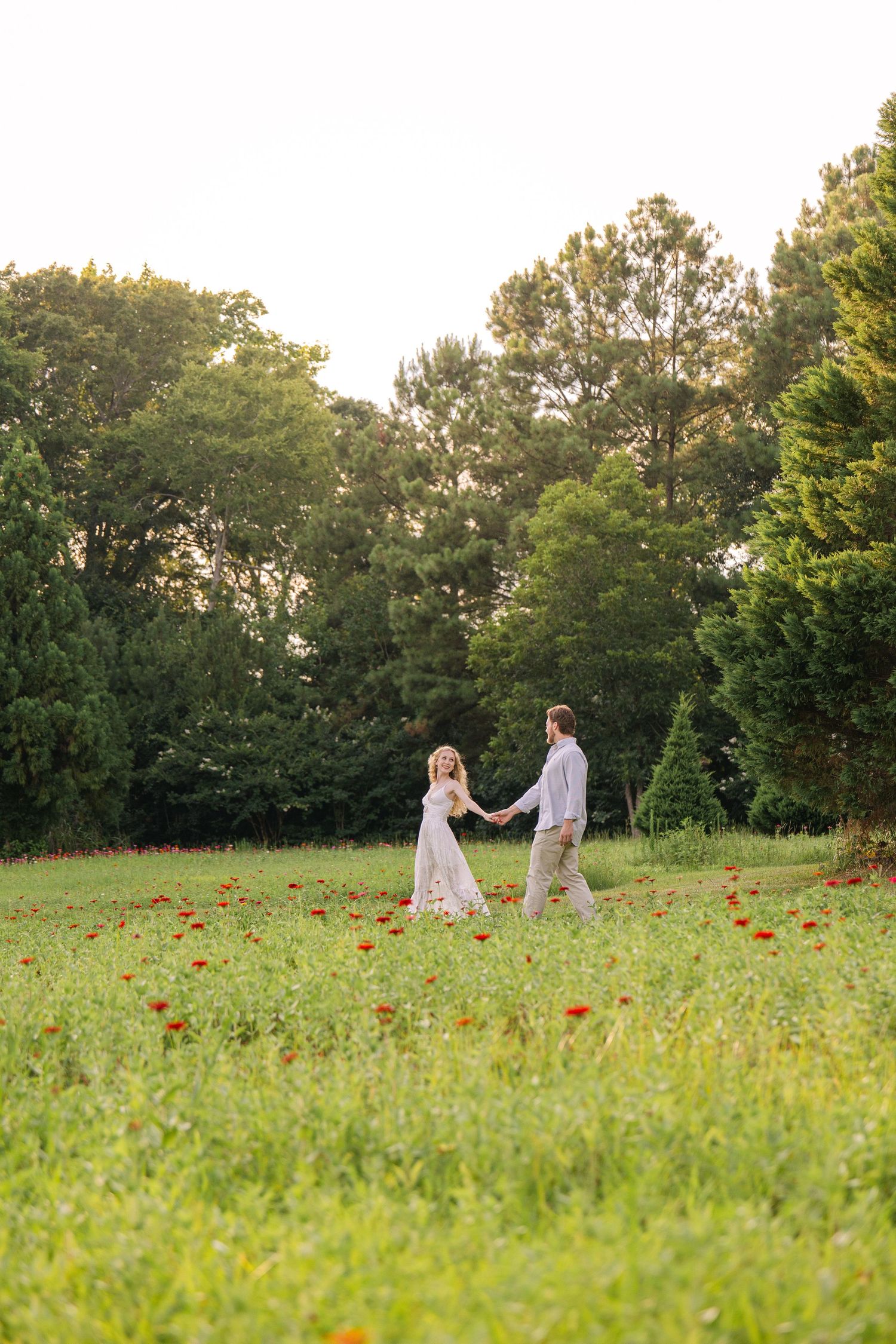 Emily and Harrison hold hands and walk through a field of zinnias at their engagement session.