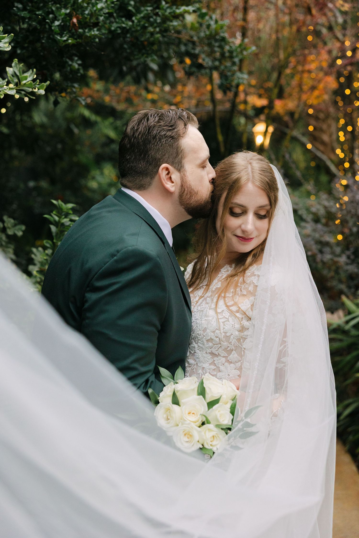 Groom kissing bride’s temple under flowing veil during romantic garden wedding at River Road and Jasmine House & Gardens in South Carolina