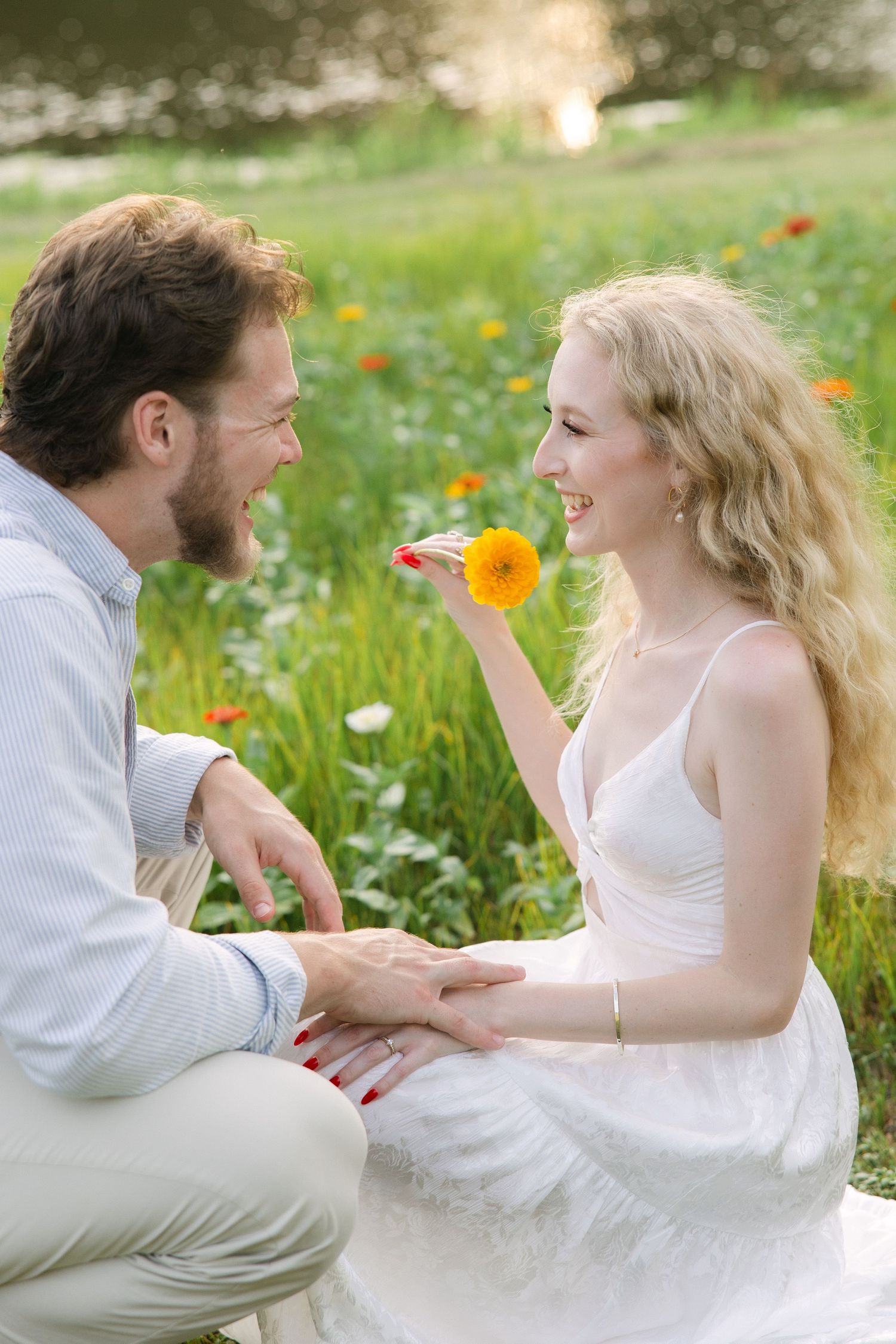 Emily and Harrison laugh and smile together during their engagement session in a flower field full of colorful zinnias in Gilbert, SC.