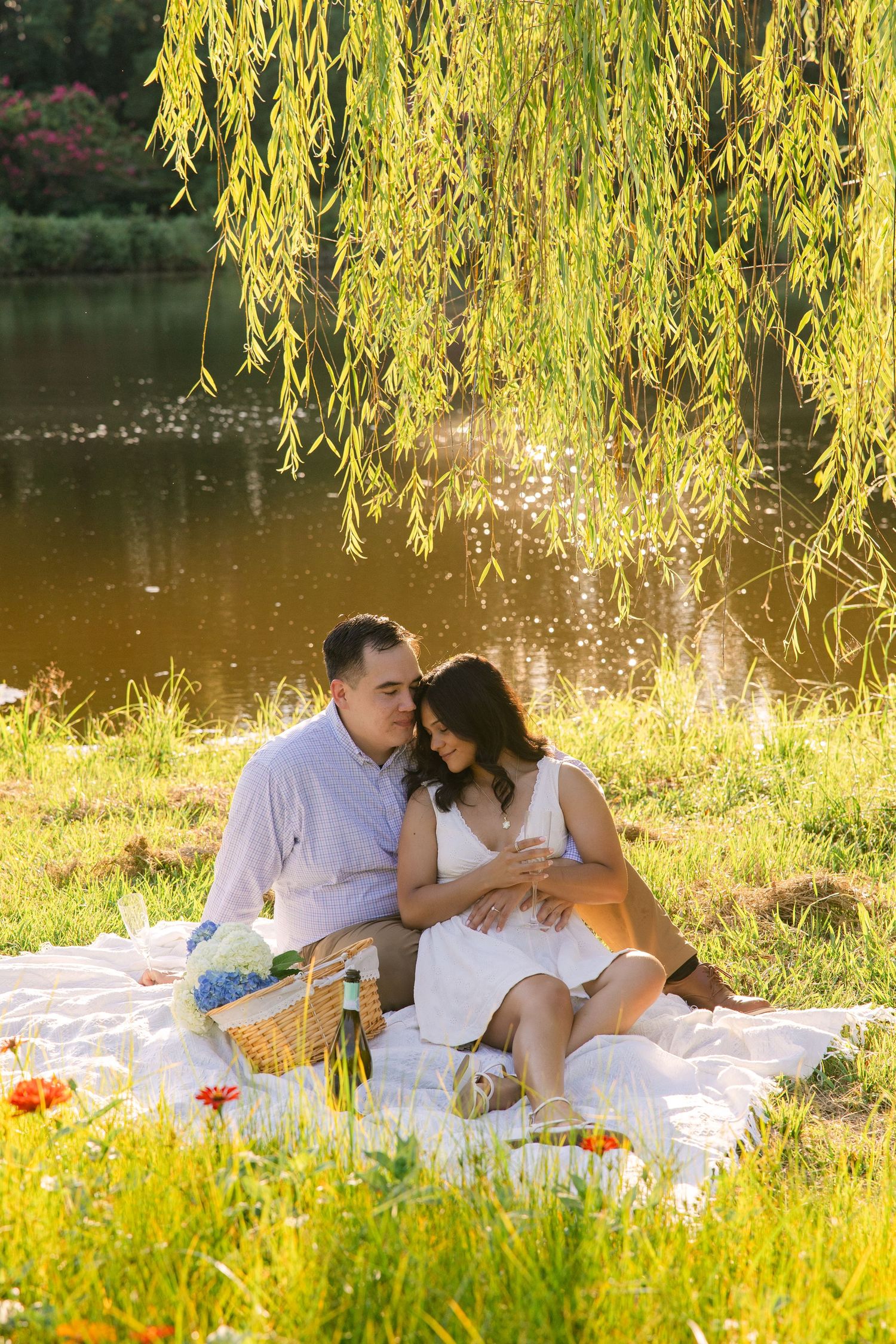 Stephanie and Matt cuddle up underneath a willow tree by a pond as they enjoy a picnic together at Hollow Creek Tree Farm in Gilbert, SC.