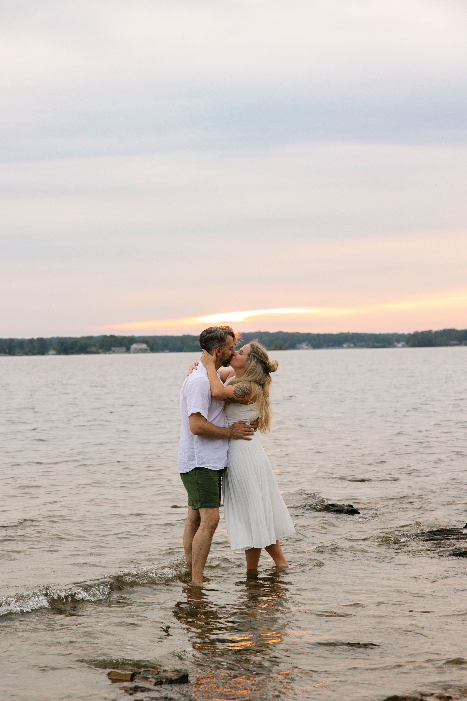 Kelly and Philip share a kiss during their engagement session on Lake Murray.  They're standing in the water right before sunset.