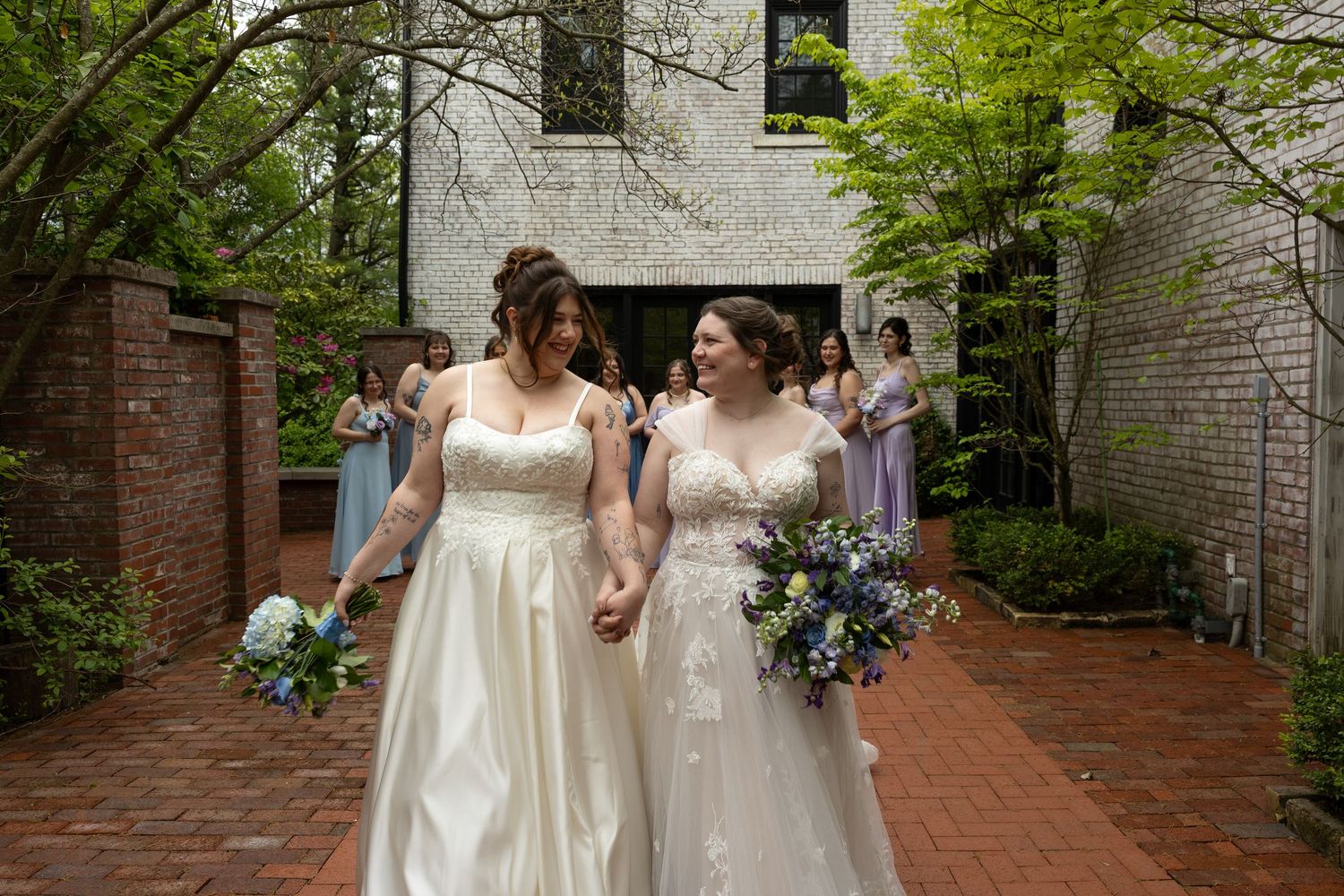 Brides smiling walking toward the camera with bouquets and bridesmaids behind them
