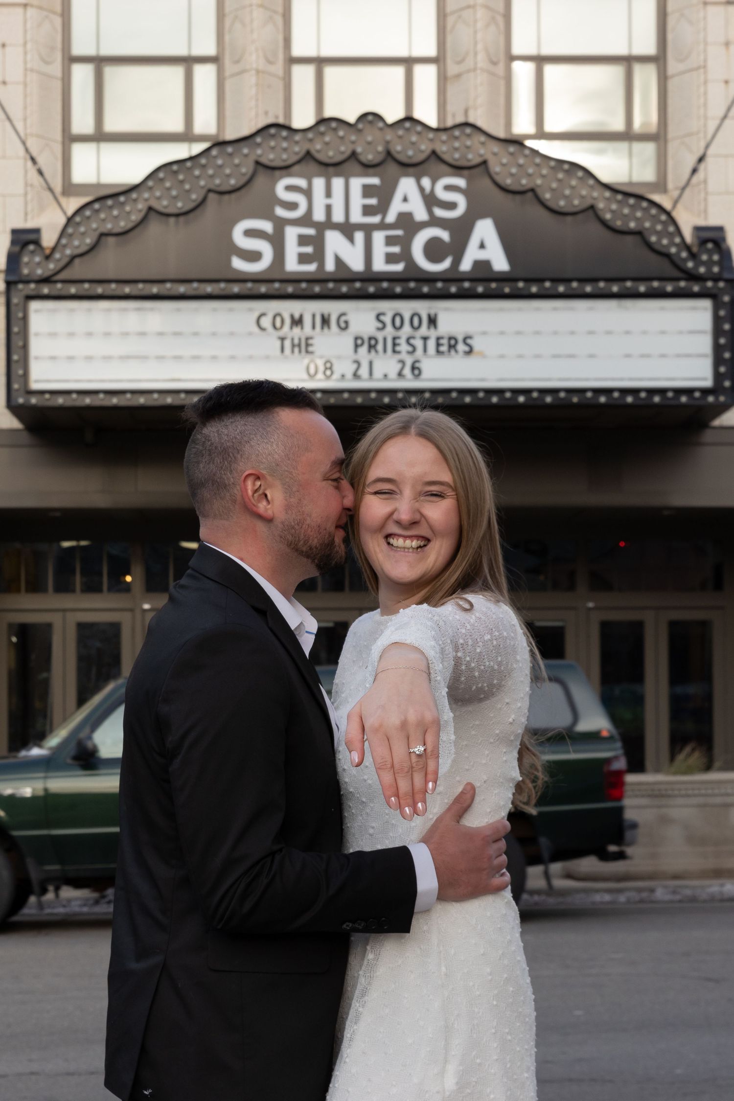 Newlywed couple embracing and showing engagement ring outside Shea's Seneca Theater marquee sign in Buffalo NY.