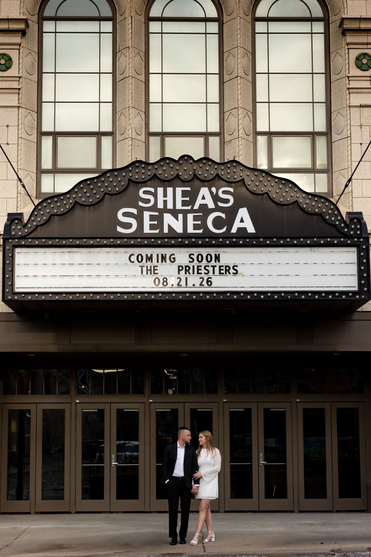 Couple poses under Shea's Seneca Theatre marquee announcing their wedding date 08.21.26 in Buffalo, NY.