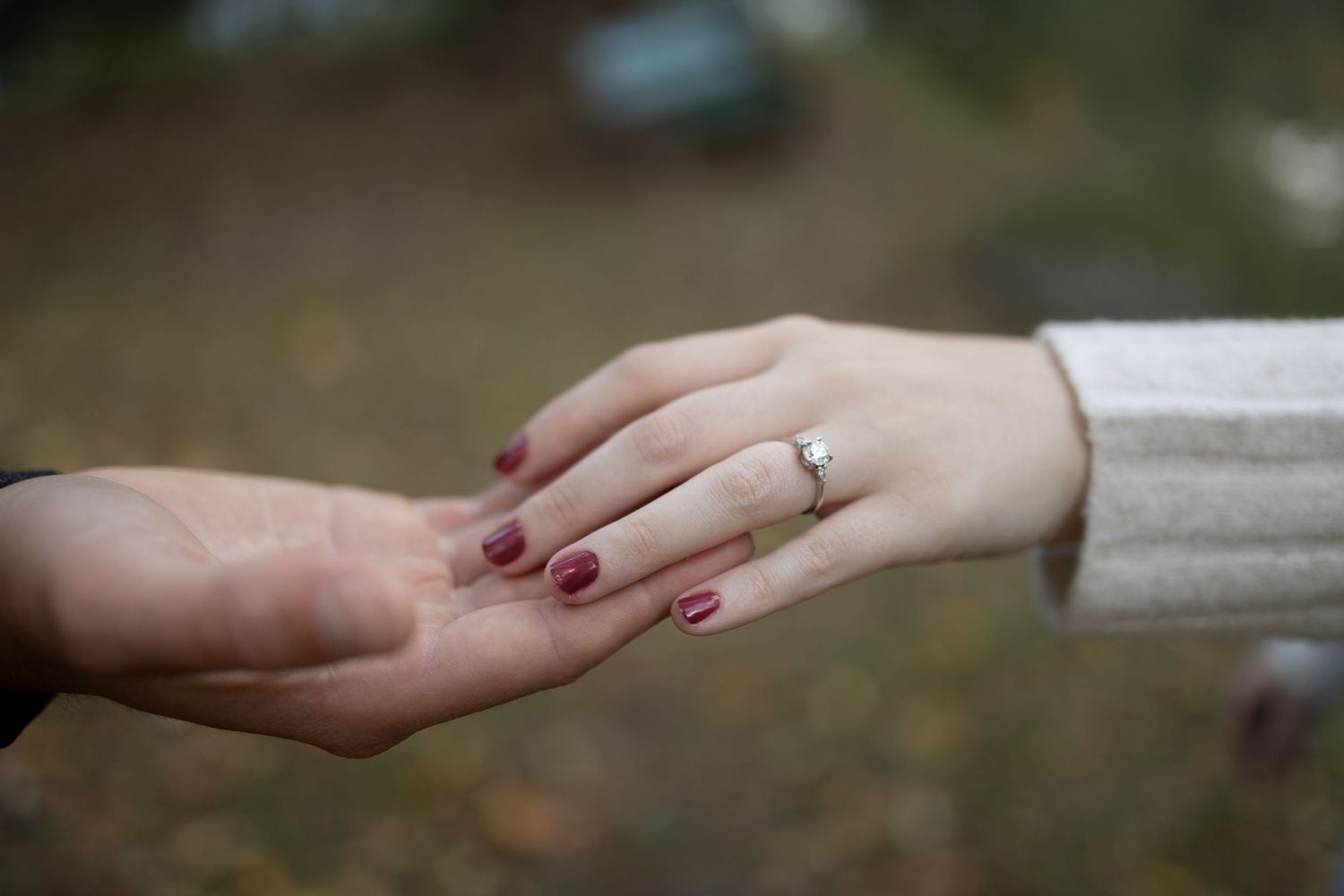 Close-up of two hands touching, one wearing a diamond engagement ring with red nail polish.
