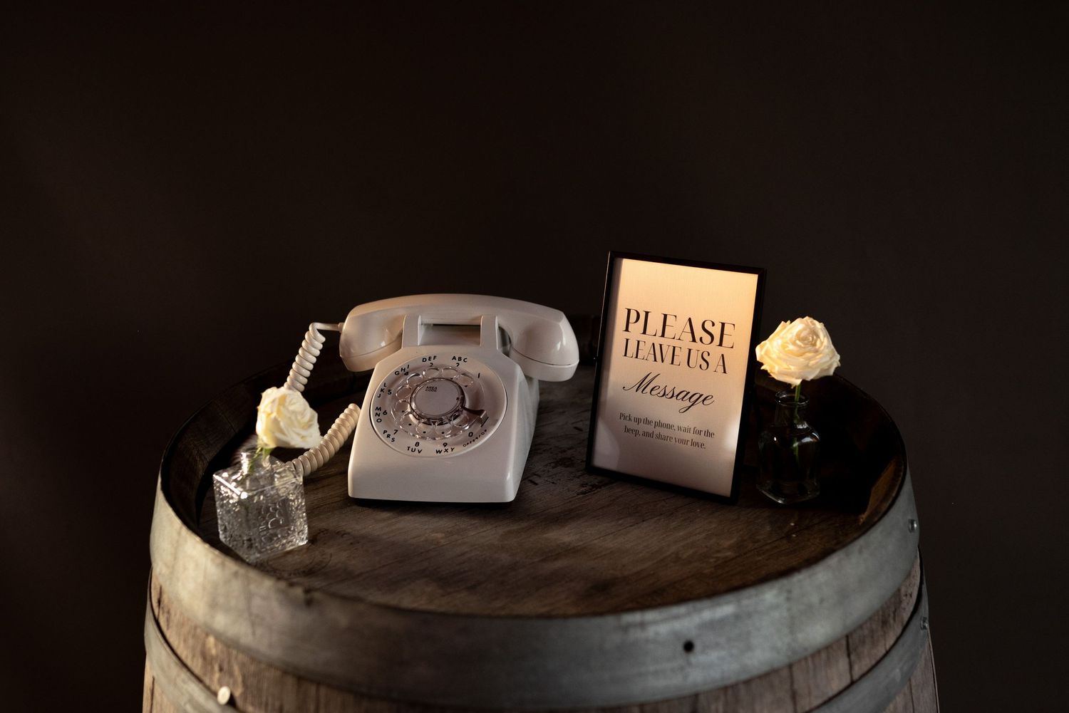 Vintage rotary phone on a wooden barrel with a please leave a message sign and floral decor for a wedding guestbook.