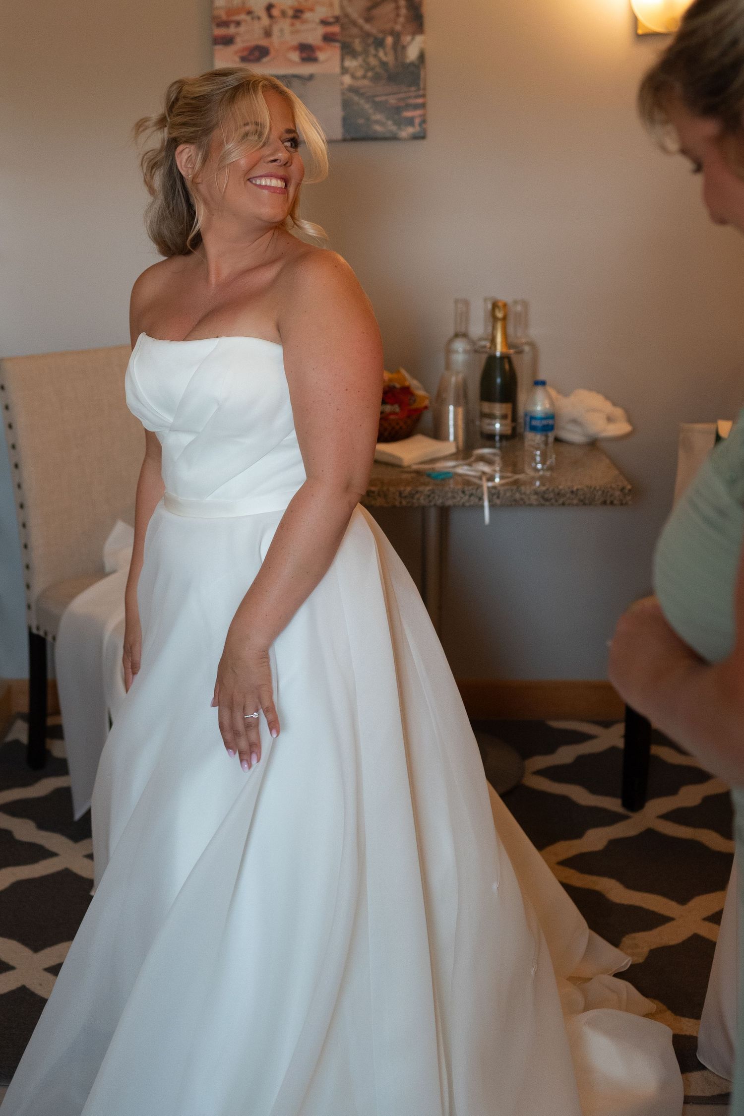 Smiling bride in a strapless white ball gown wedding dress getting ready in a hotel room.