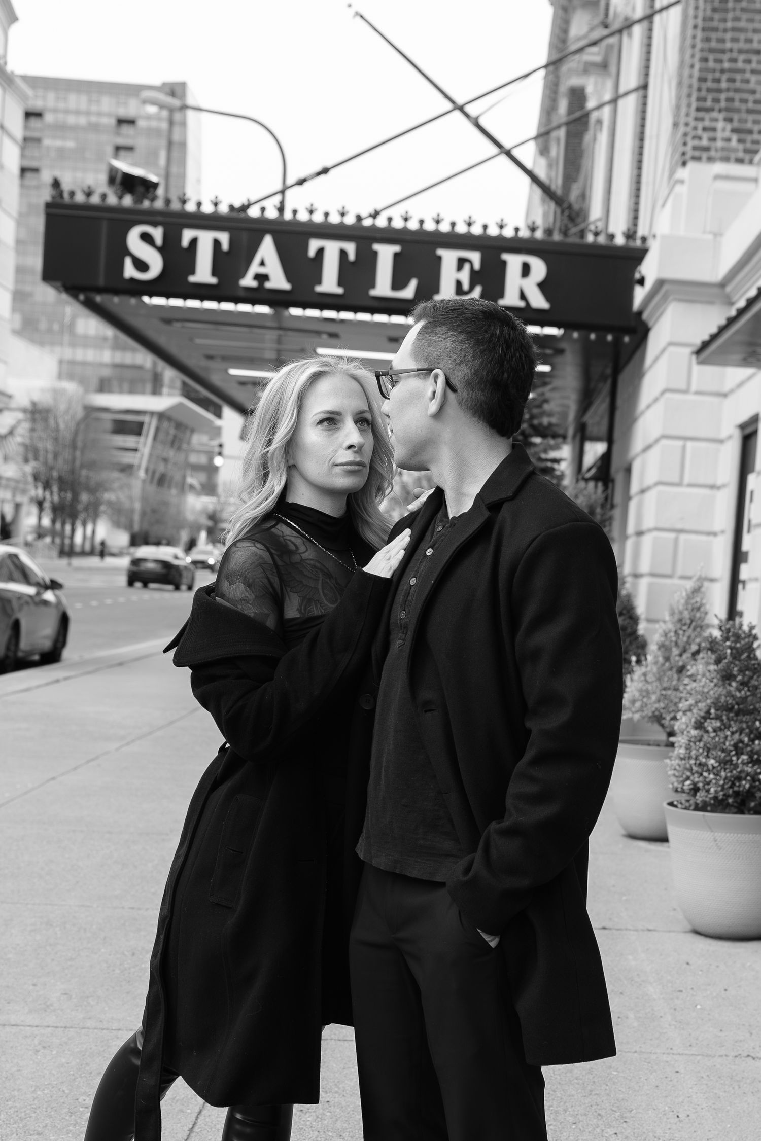 Black and white photo of a couple in black coats standing outside the Statler hotel on a city street in Buffalo New York