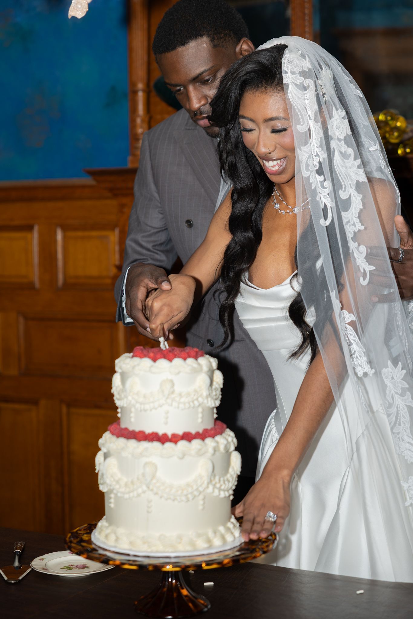 Bride and groom cutting a two-tier white wedding cake decorated with red berries at their wedding reception.
