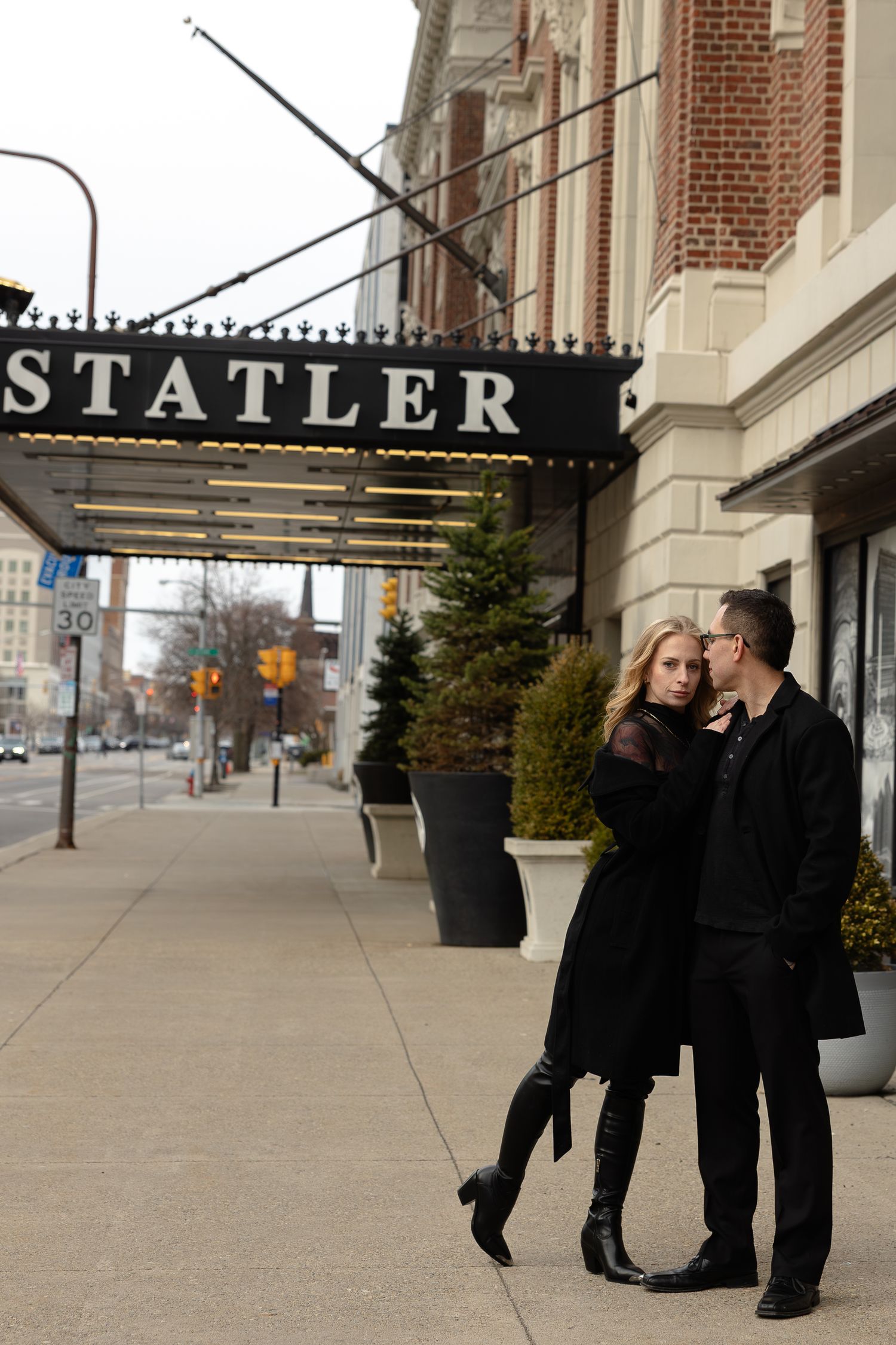 Couple in black outfits posing outside the Statler Hotel on a city sidewalk in Buffalo New York